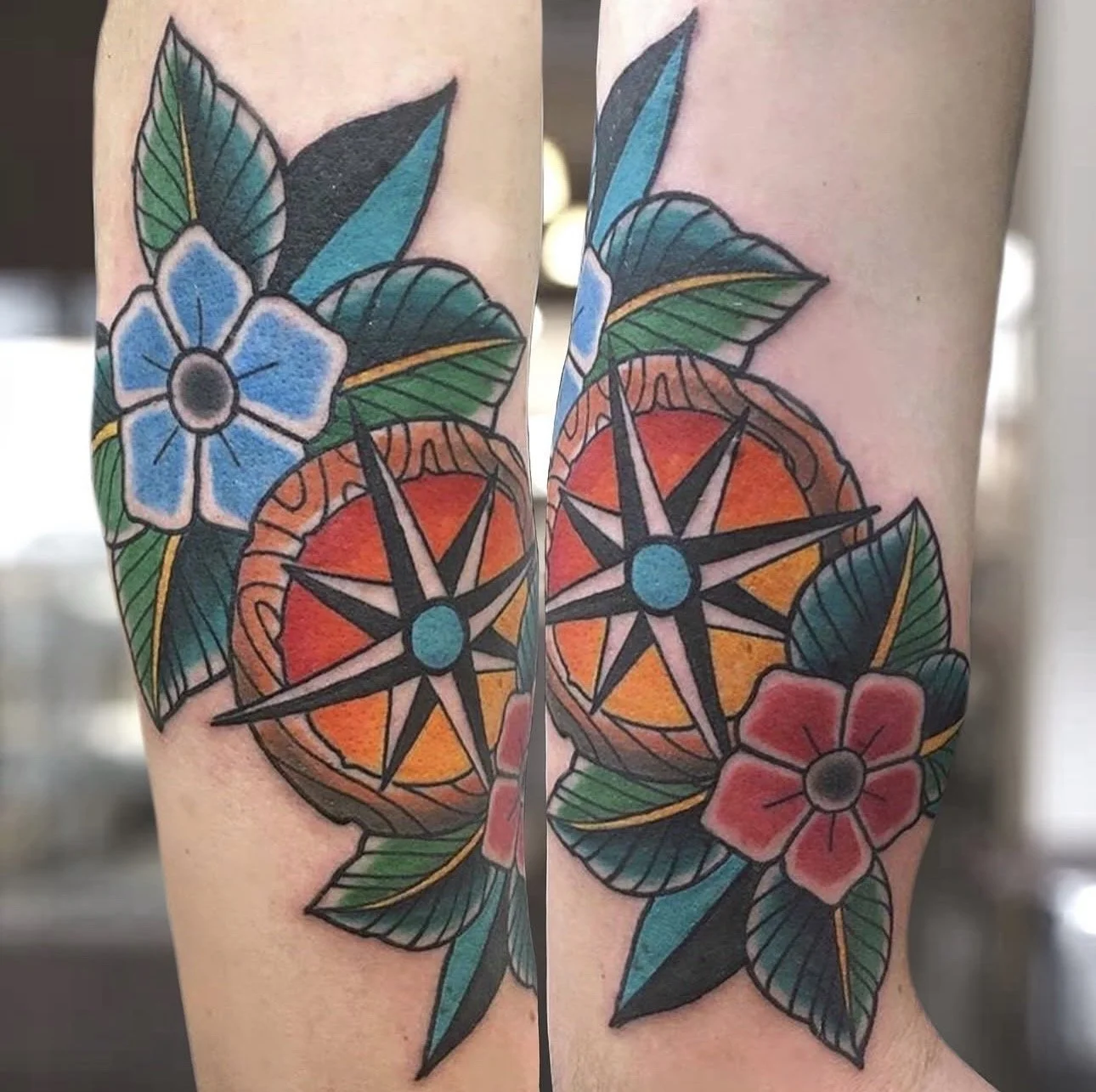 Tattoo of a compass surrounded by blue and red flowers and green leaves on a person's arm.