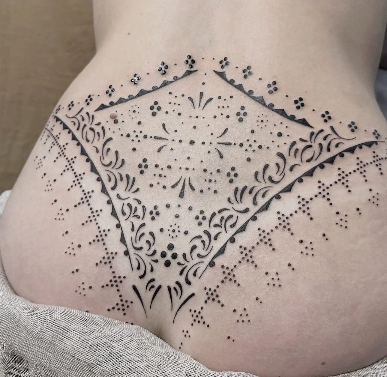 Feminine tattoo of a geometric and floral design on person's back.
