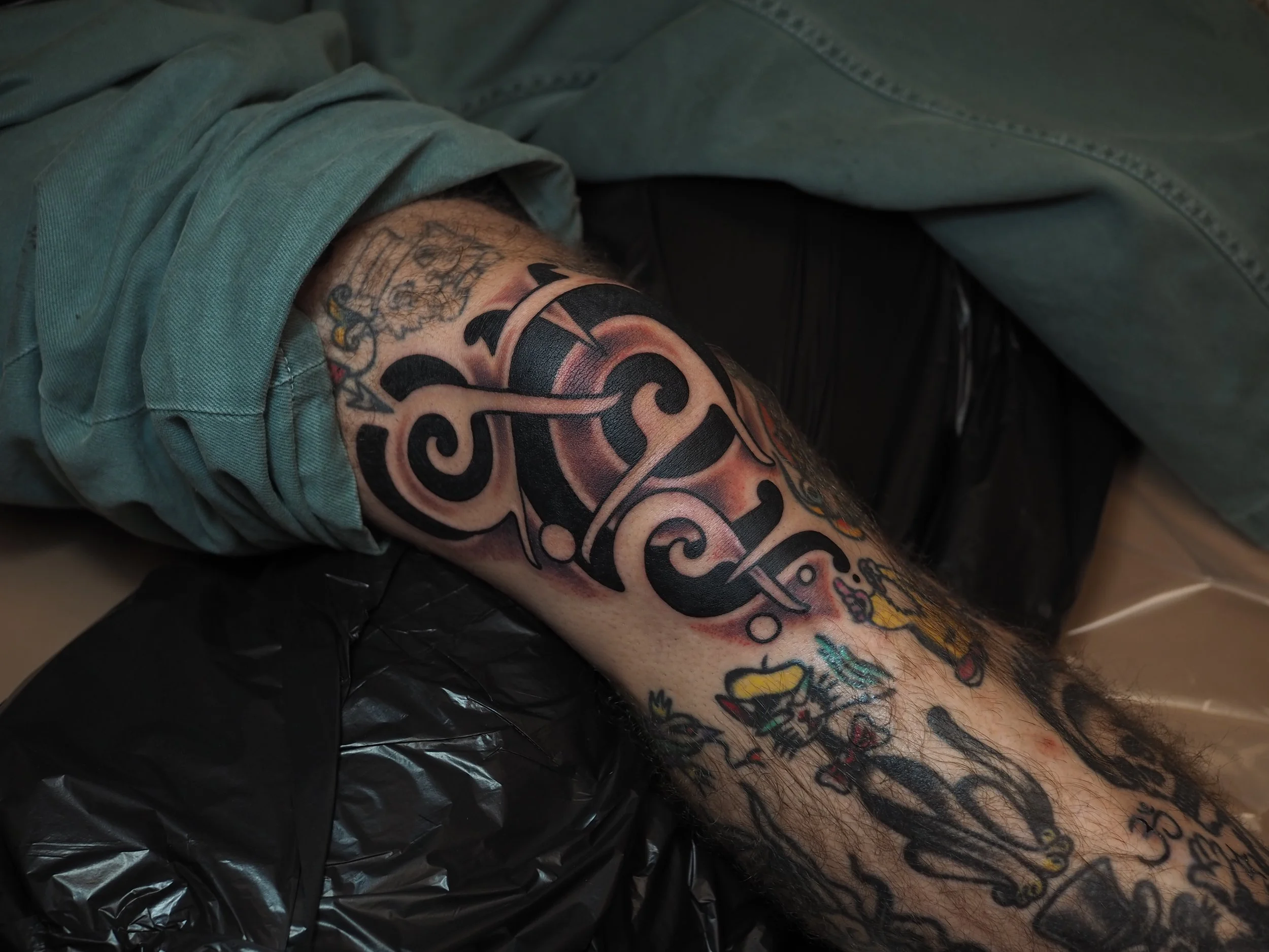 Tattooed leg with tribal tattoos, wearing rolled-up green pants, resting on a black pillow.