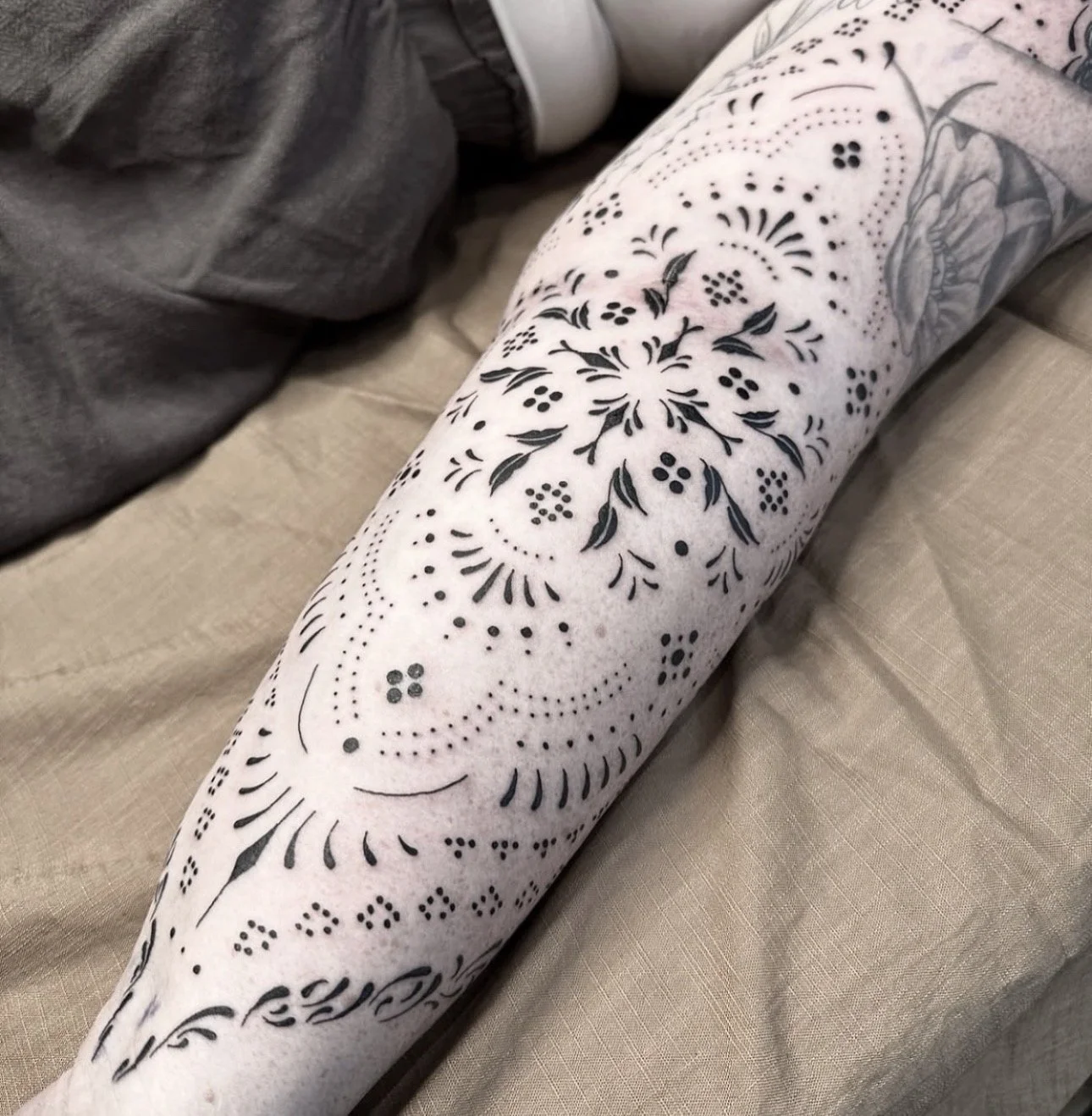 A person's arm with black tribal-style tattoo designs, including floral and geometric patterns, on light skin.