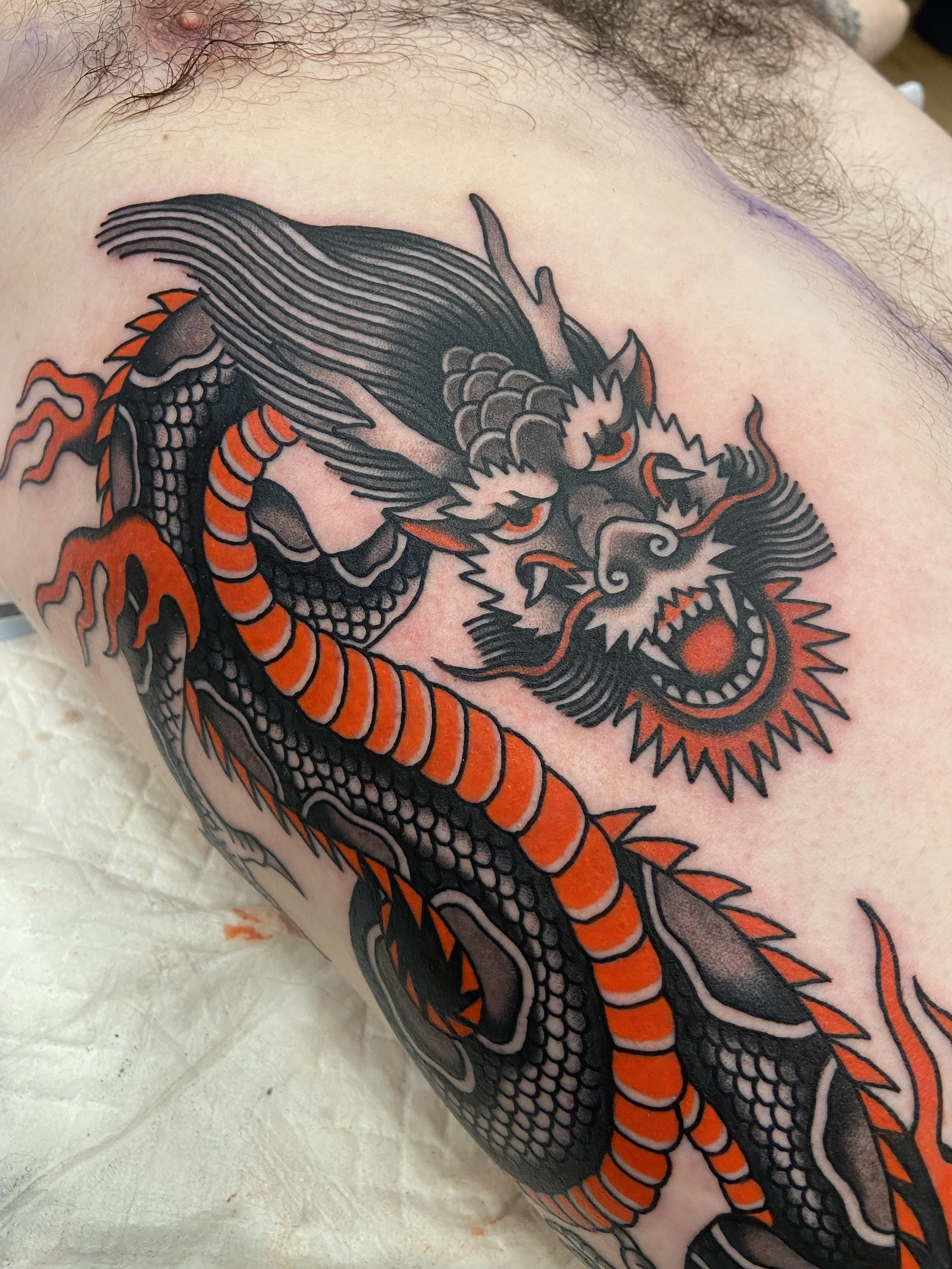 Tattoo of a fierce stylized dragon with black and orange details, showing its head and part of its coiled body.