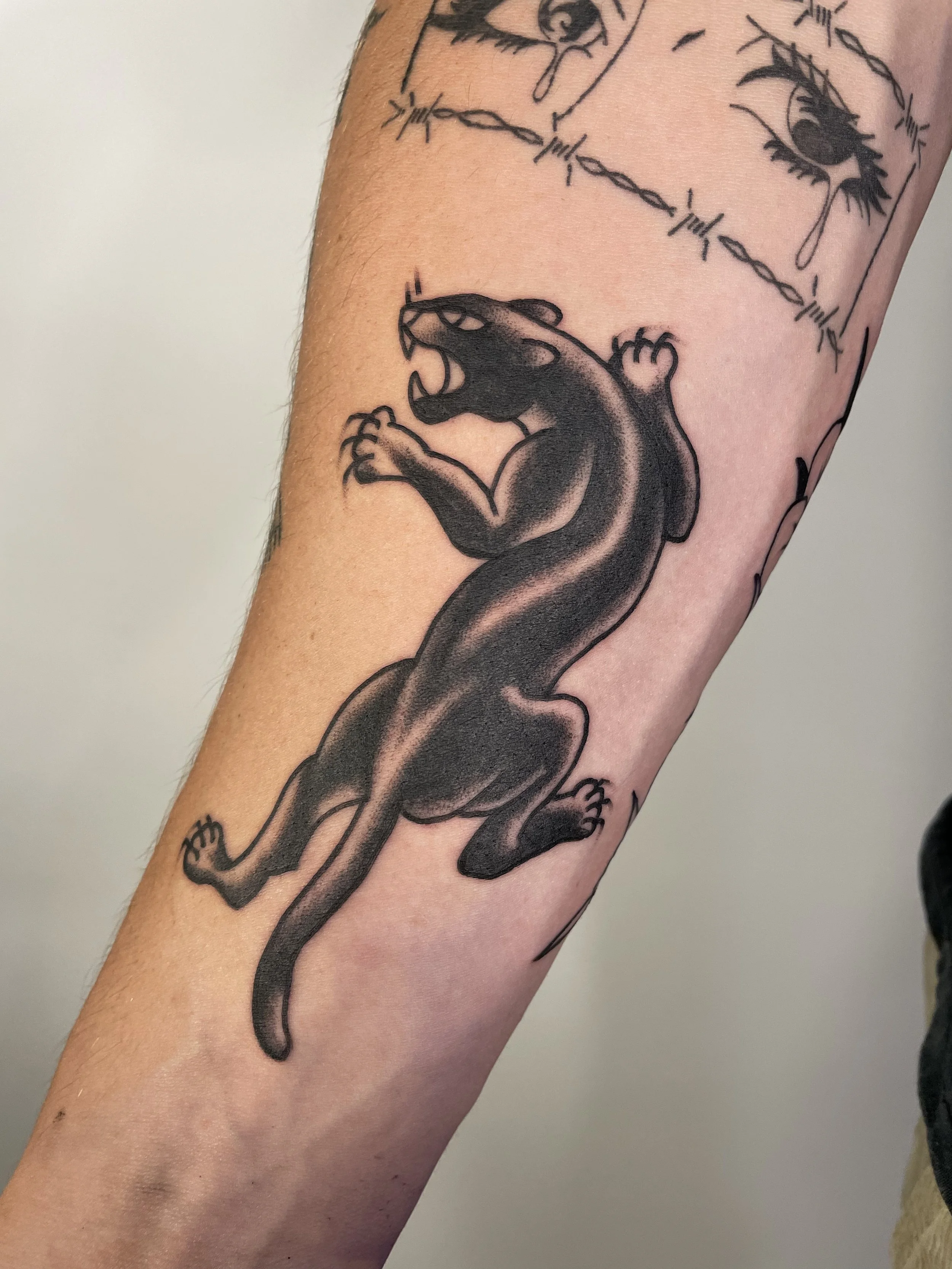Tattoo of a black panther in a jump position with claws extended, on an arm.