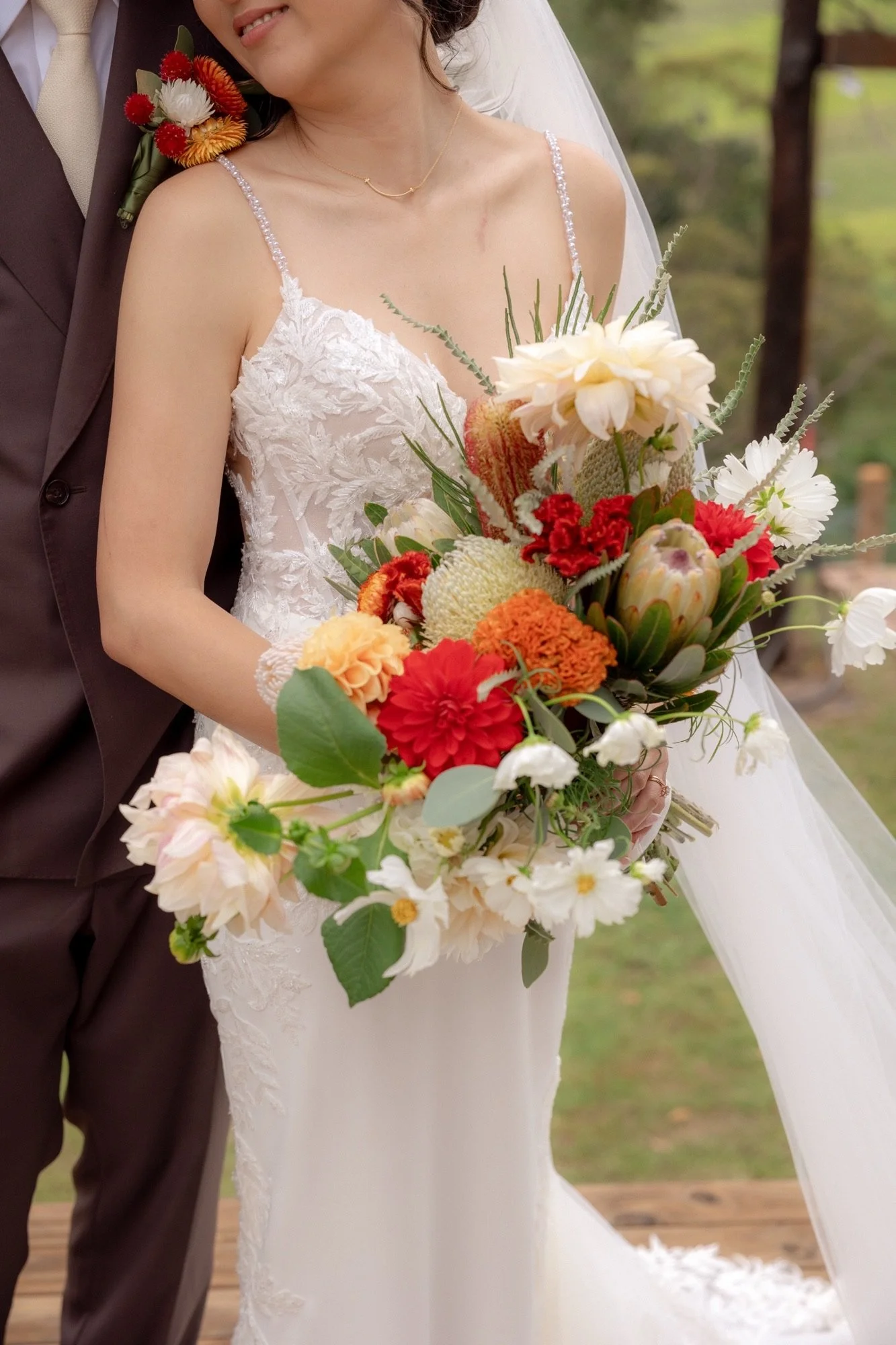 Bride holding a bouquet of red, orange and white native flowers beside the groom at Kingaley Farm Stay