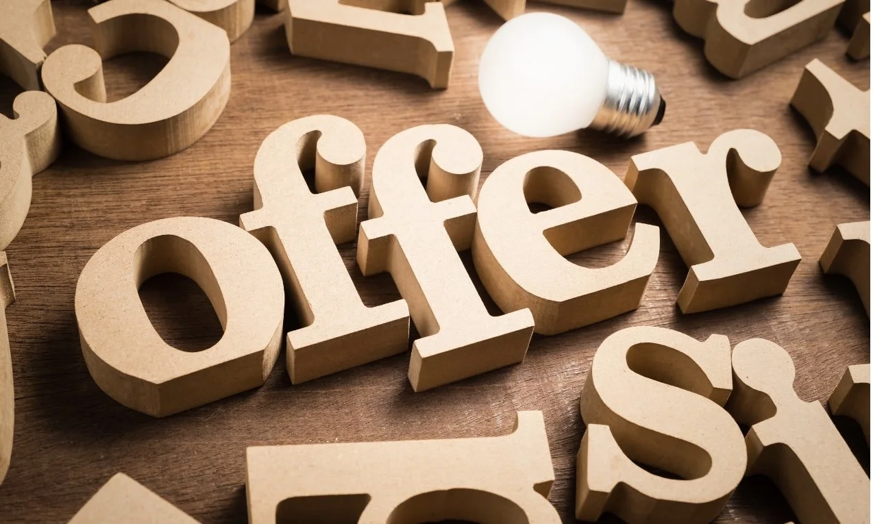 Wooden letters spelling the word 'offer' on a wooden surface with a light bulb nearby.