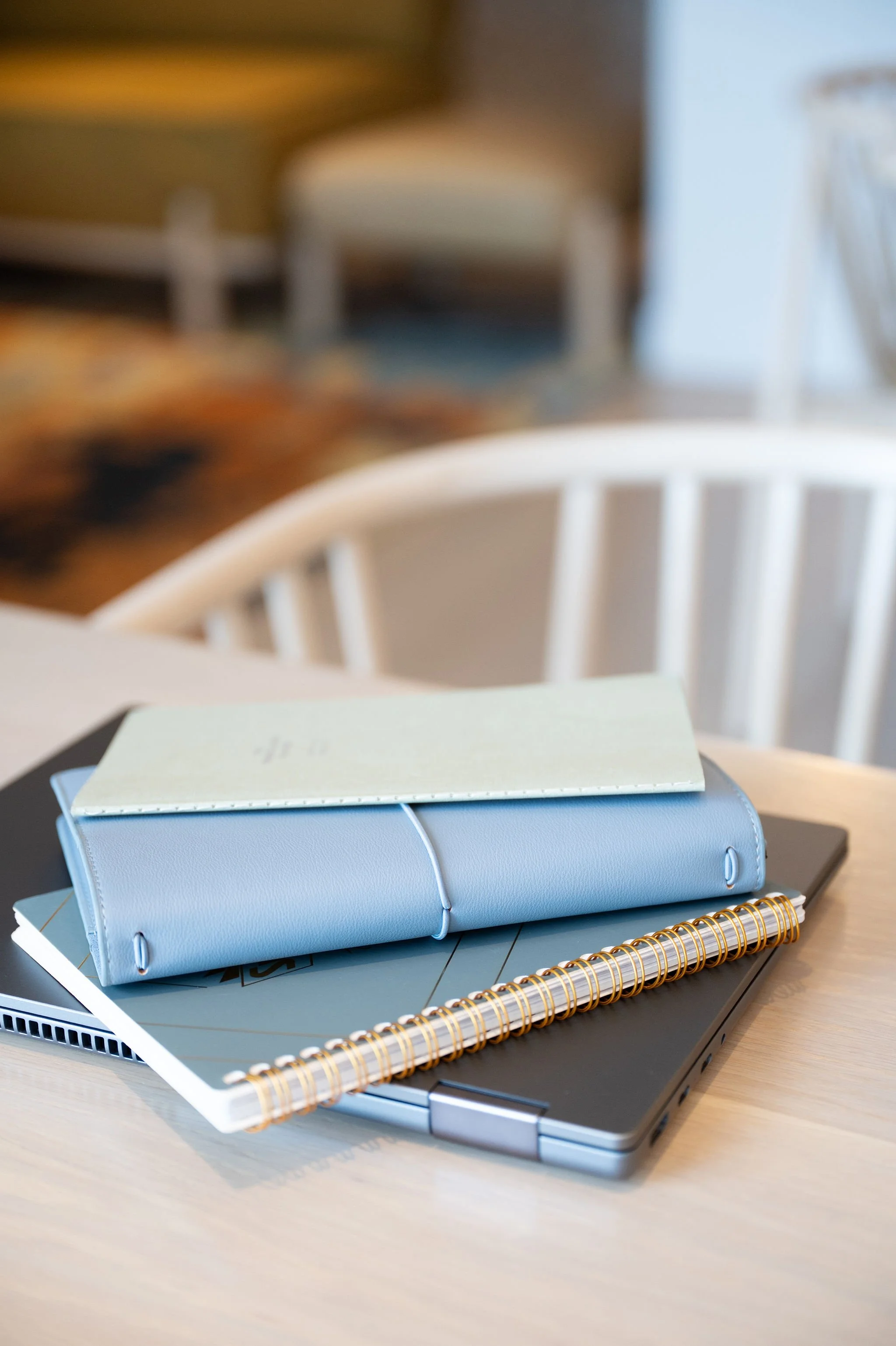 A light blue binder, a black notebook, a open spiral-bound notebook, and a closed laptop on a desk.