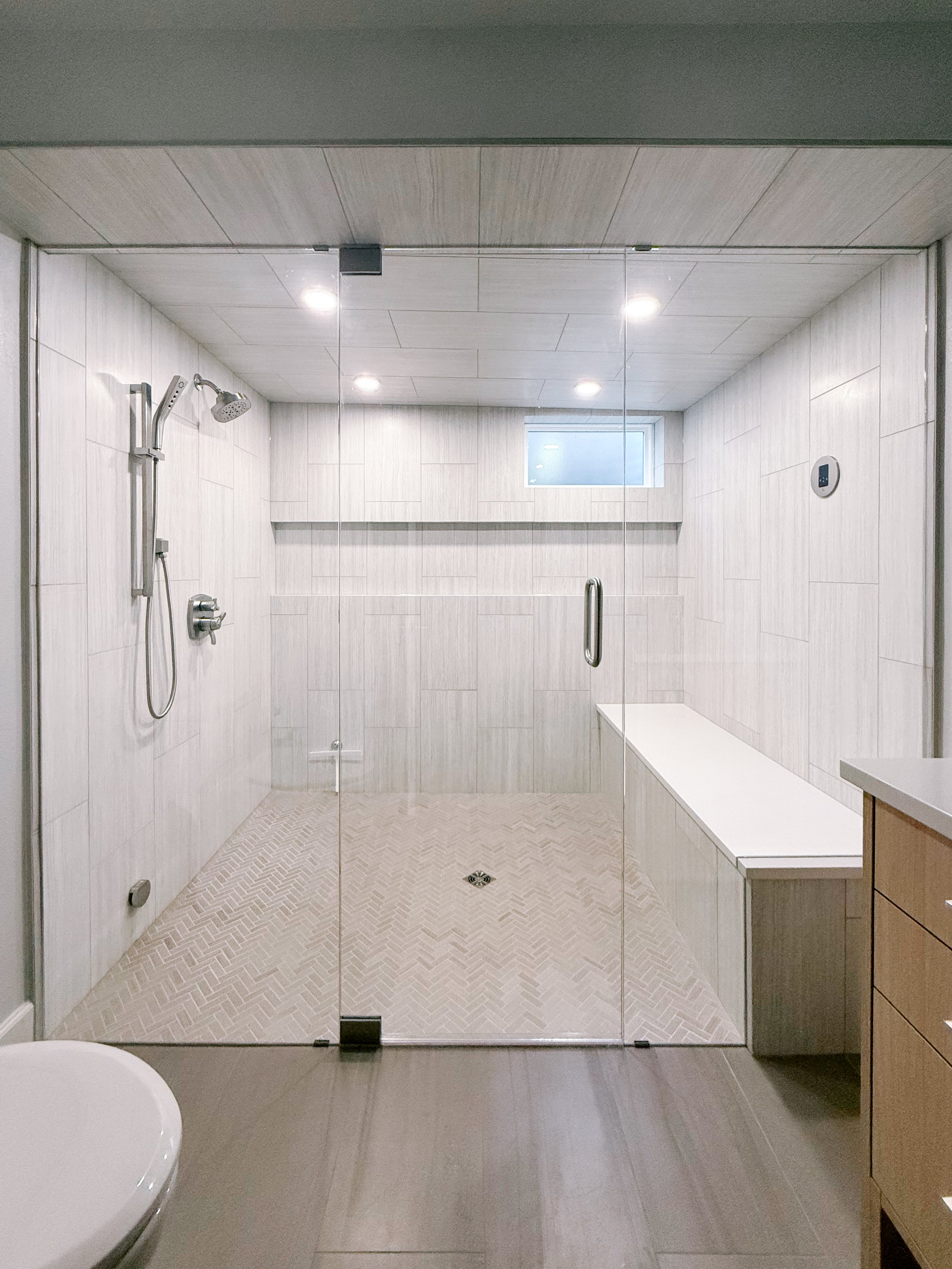 Modern bathroom with glass-enclosed curbless entry steam shower, tiled walls, mitered niche, built-in bench, dimmable lighting.