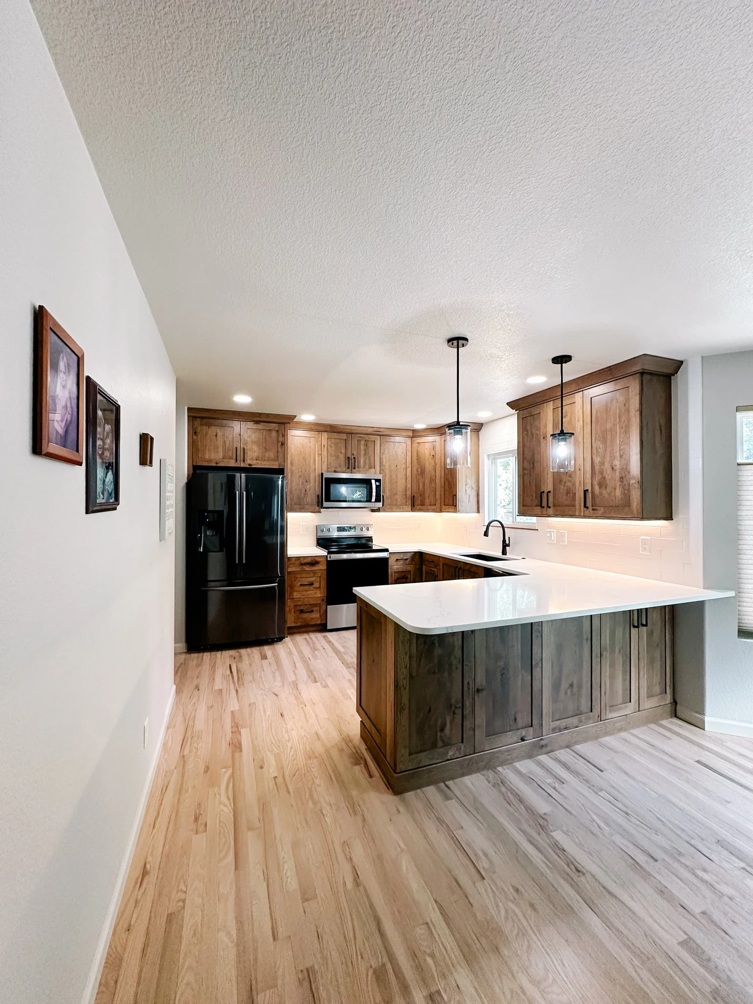 Modern kitchen with wooden cabinets, black appliances, white countertops, and pendant lighting.