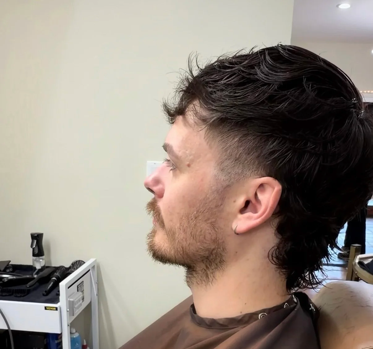 Side profile of a man with a fresh haircut and styled dark hair, sitting in a barber's chair.