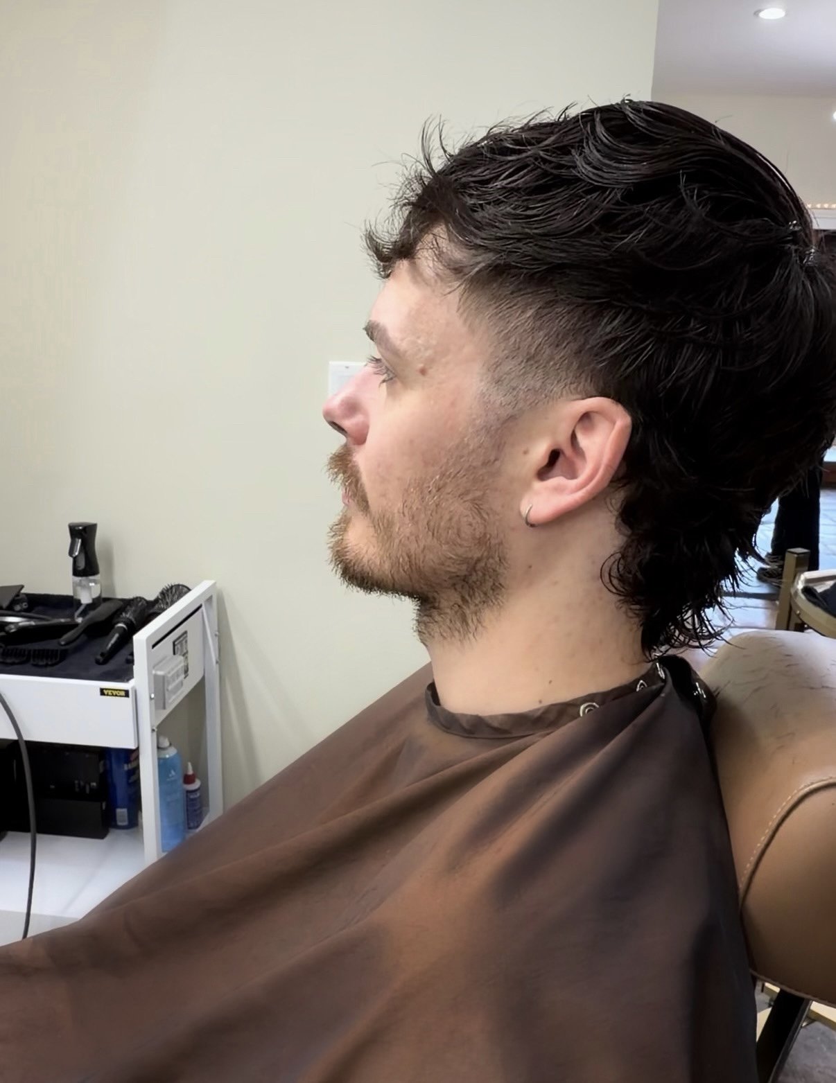 Man sitting in a barber chair at a salon with a fresh haircut, viewed in profile.
