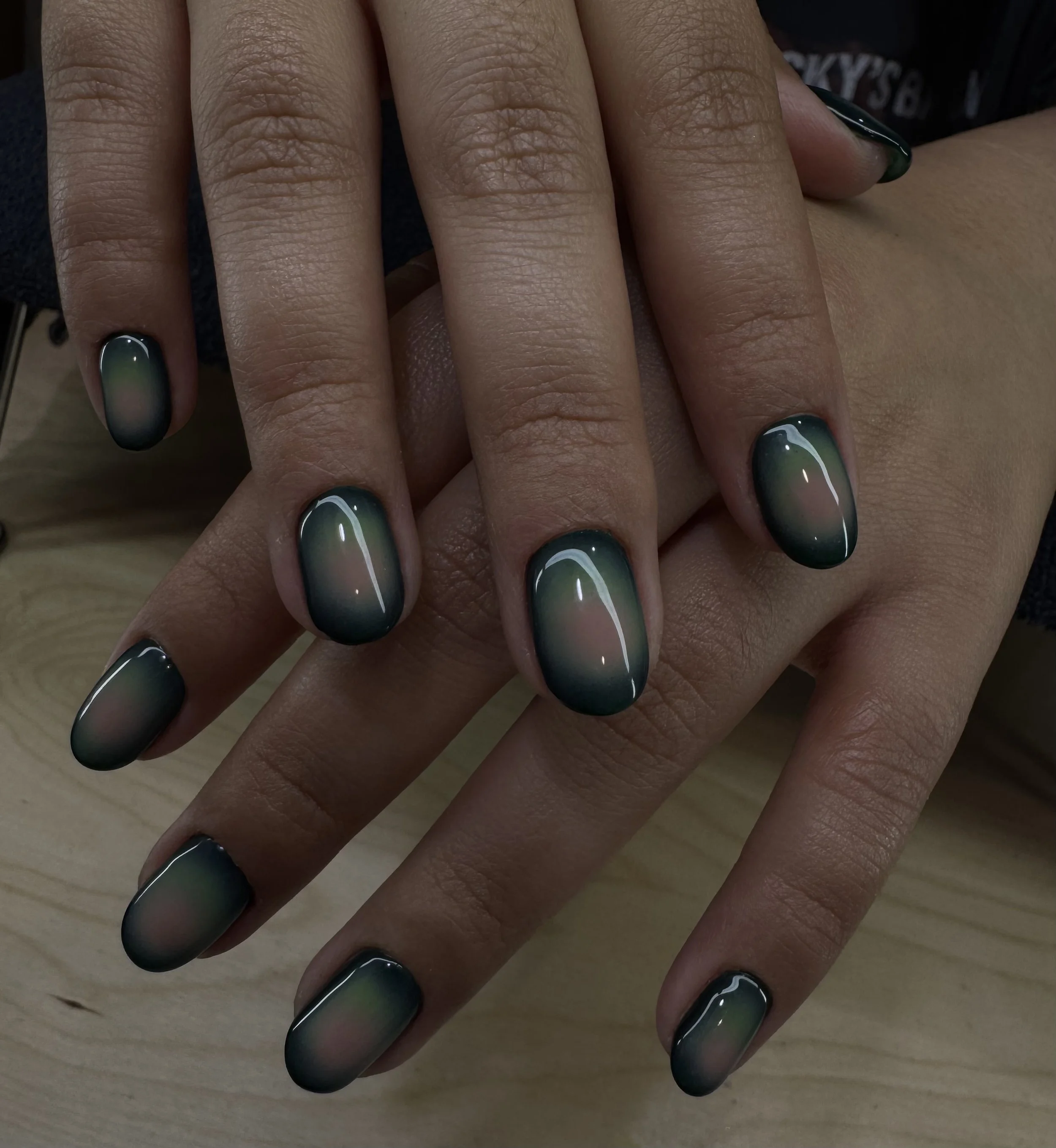 Close-up of a person's hand displaying freshly painted nails with an ombre green and black nail art design.