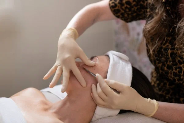A woman receiving a cosmetic facial injection from a professional wearing gloves, with a towel wrapped around her head