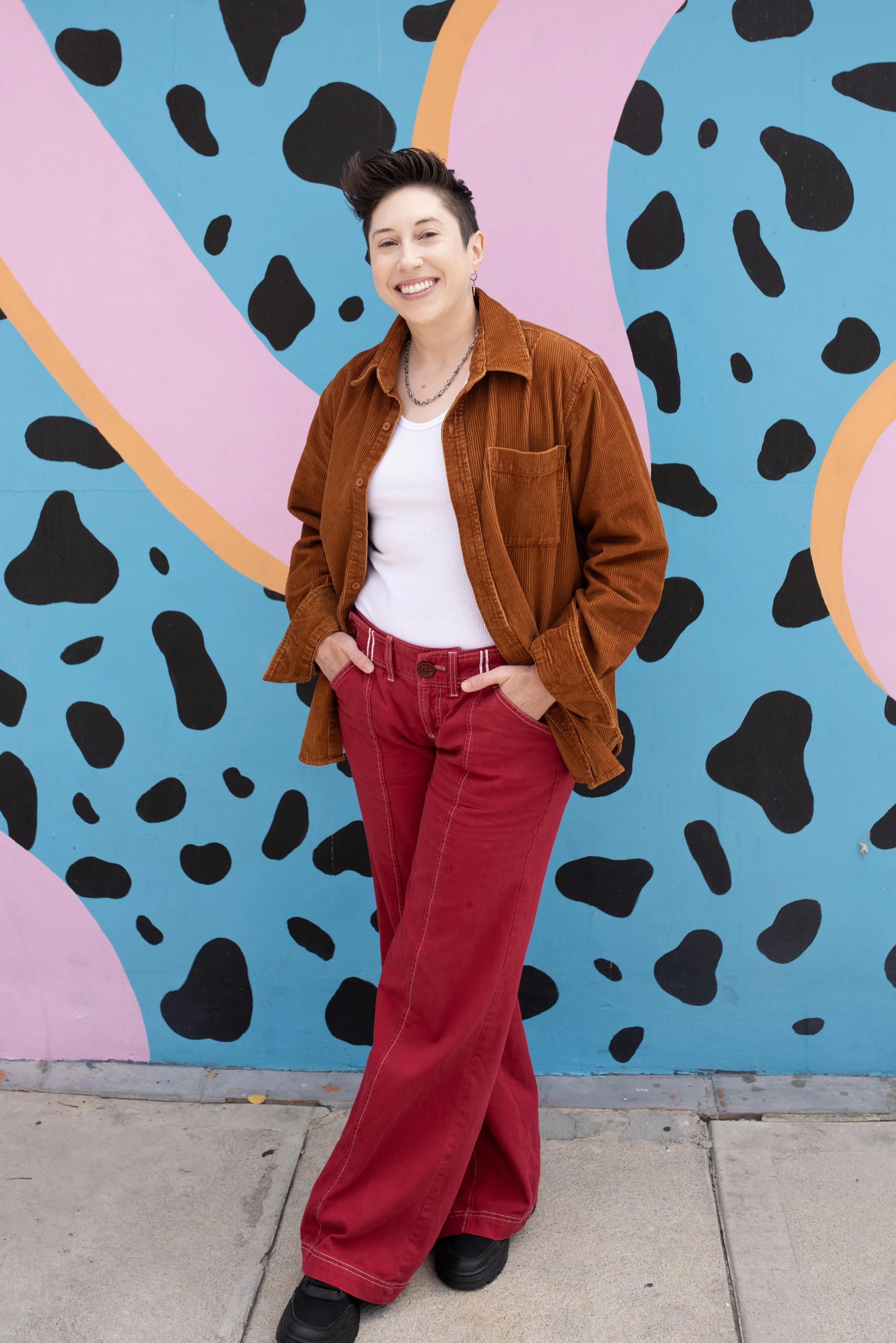 Person standing in front of a colorful, abstract mural with black spots on blue, pink, and orange background.