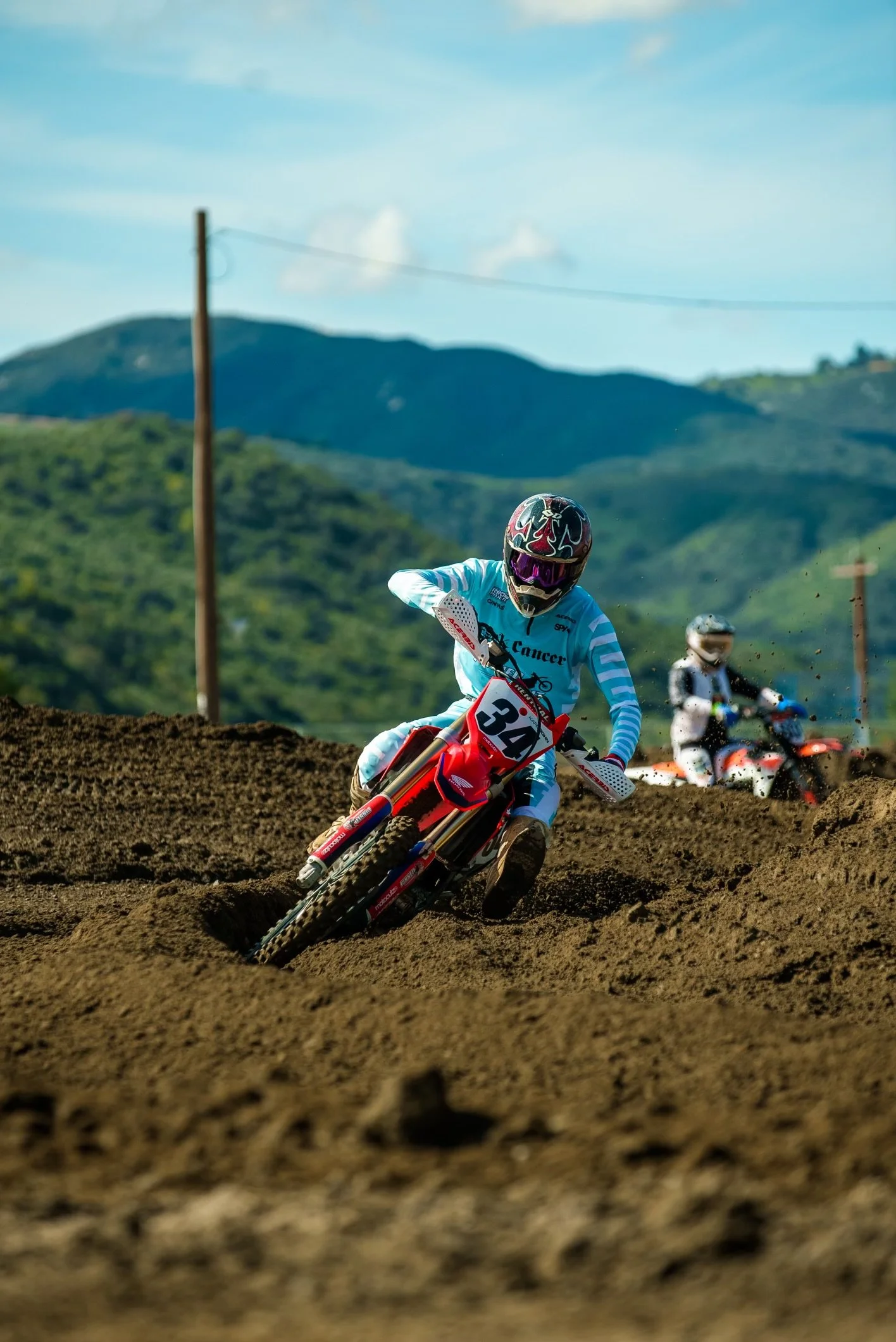 Motocross rider at Fox Raceway wearing a blue and white outfit and helmet, with mountains and a blue sky in the background.
