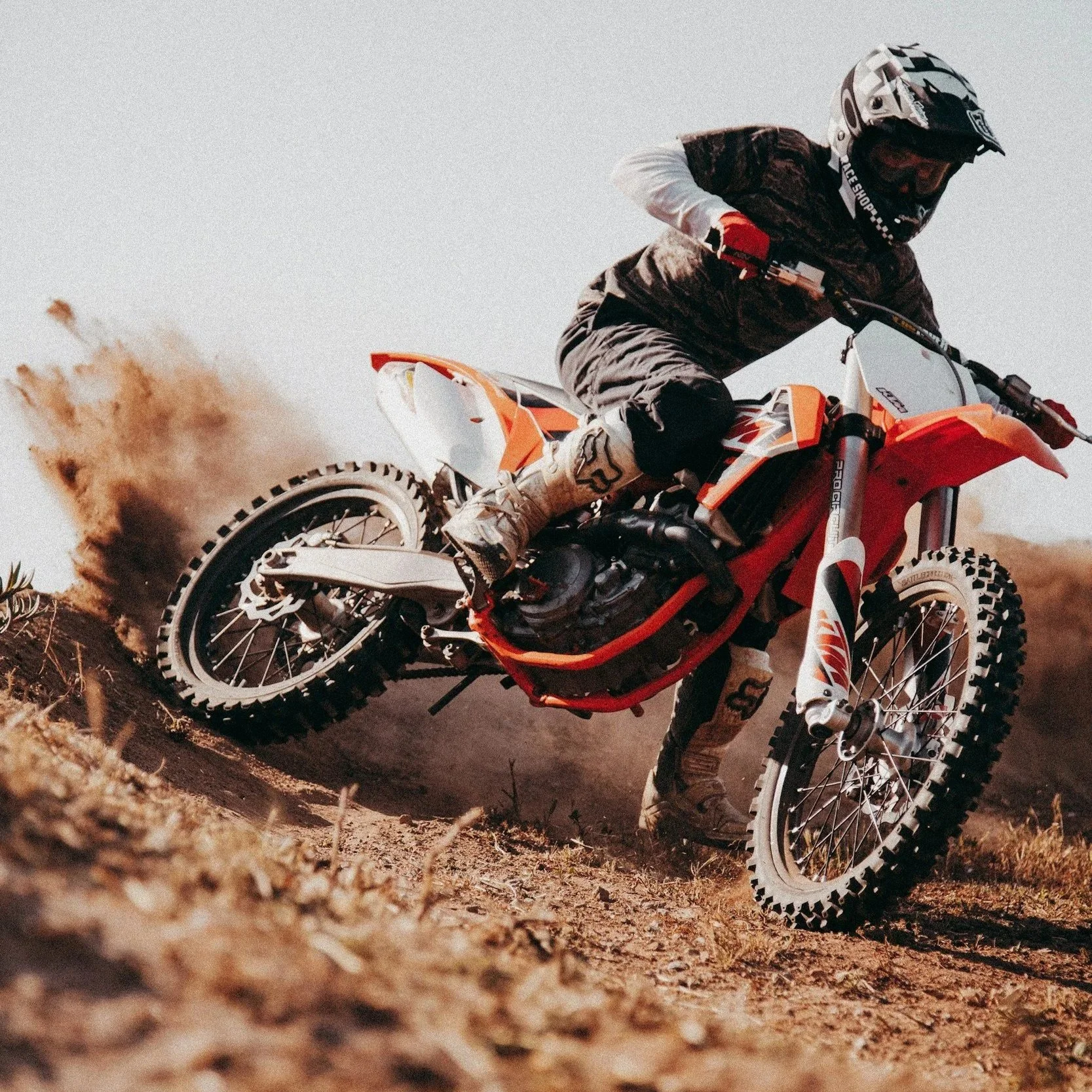 Motorcycle rider in motocross gear riding a dirt bike on a dirt trail, kicking up dust as they navigate a turn.