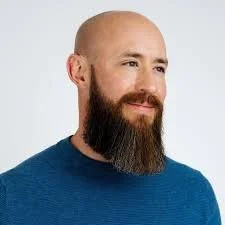 Dr. Steve Thayer, CEO. A man with a full beard wearing a blue sweater, looking to the side with a neutral expression, against a plain light background.