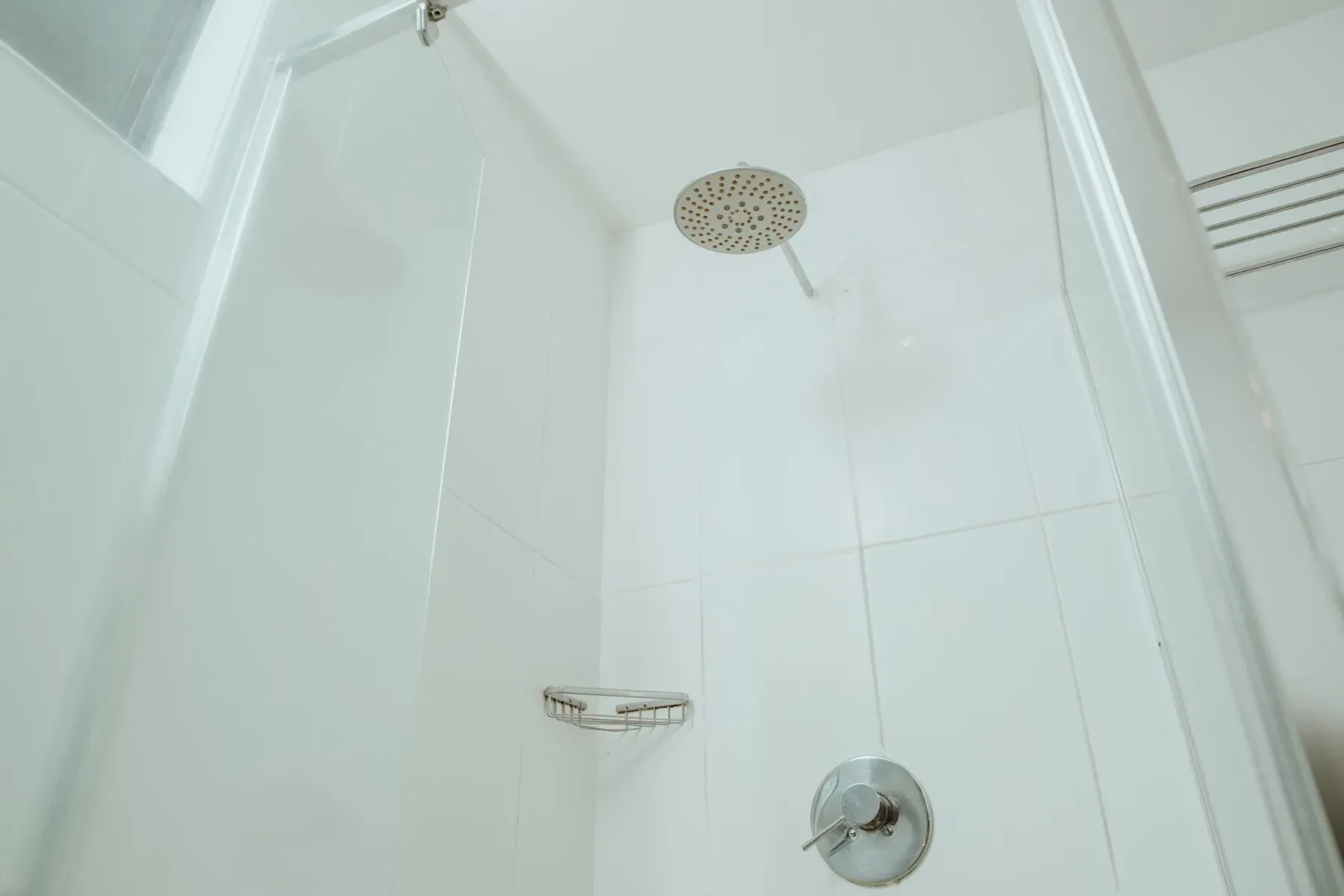 Showerhead and shower controls inside a shower stall with white tiled walls.