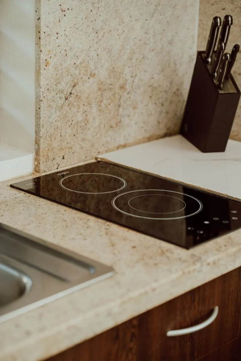A kitchen countertop with a black electric cooktop that has two burners and a knife block with several knives on a nearby black holder.