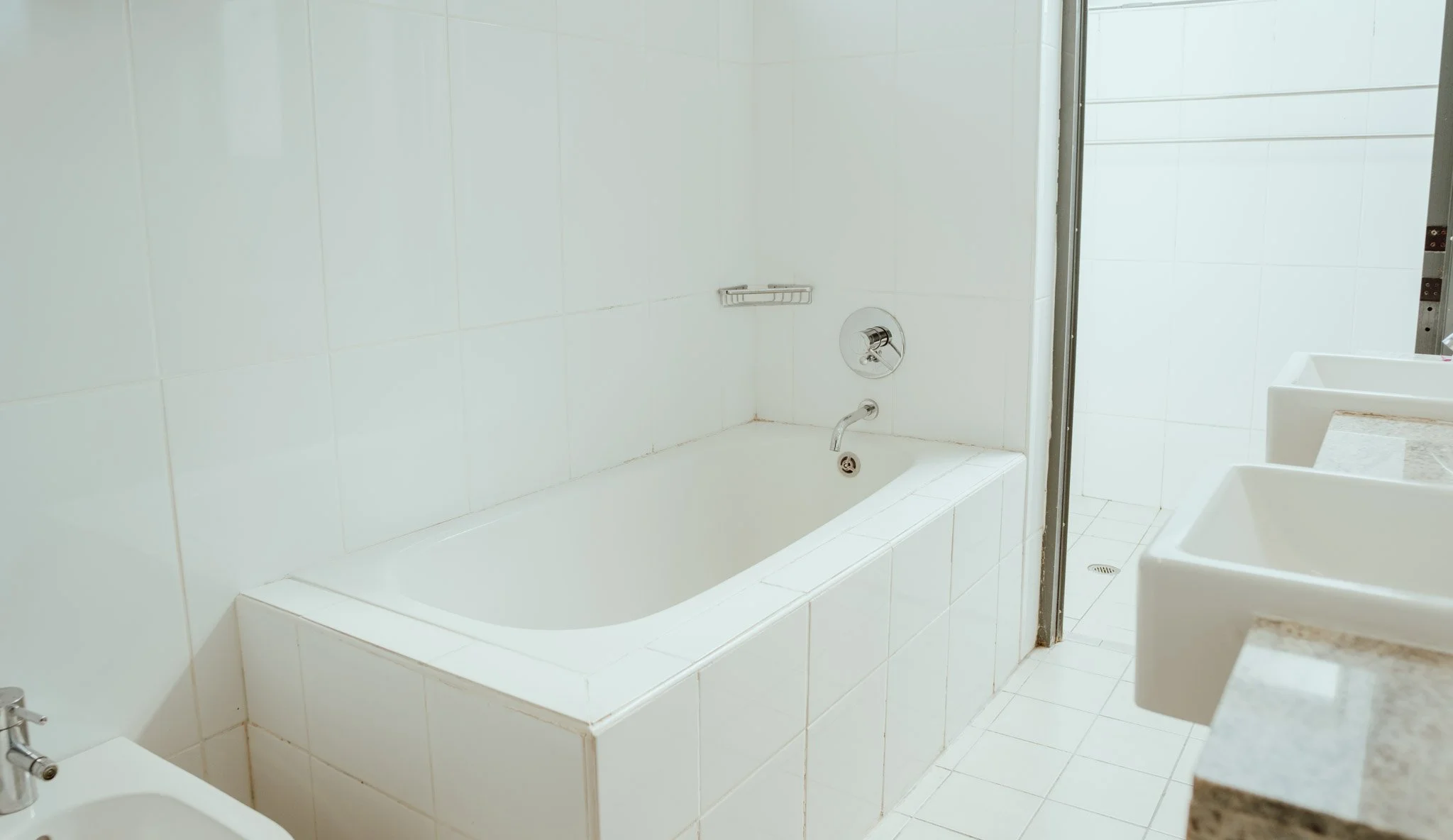 White bathroom with bathtub, sinks, and shower area.