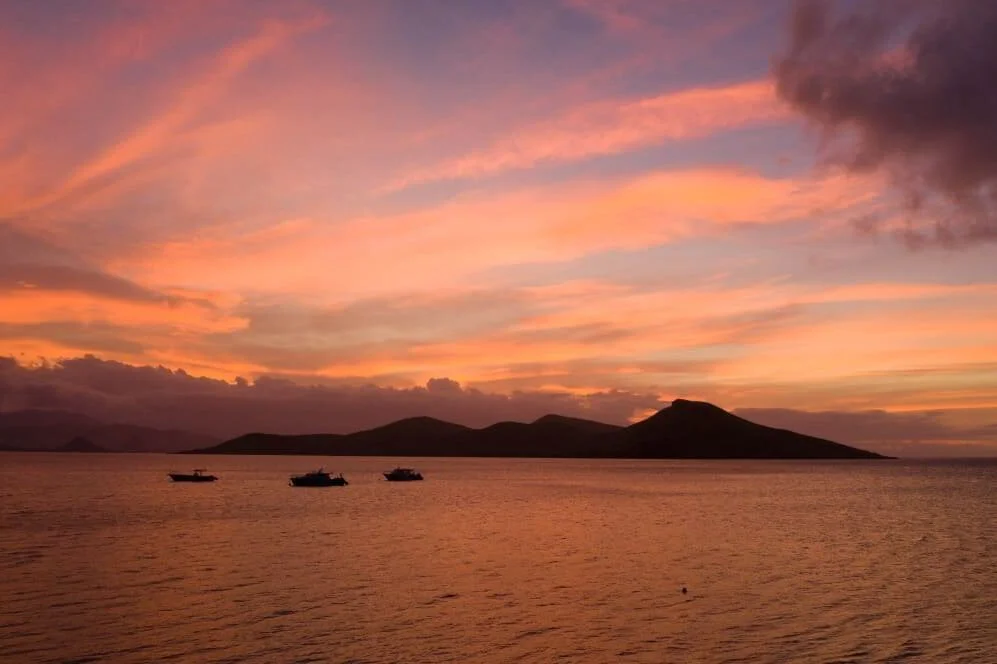 Sunset over the ocean with a silhouette of islands and three boats