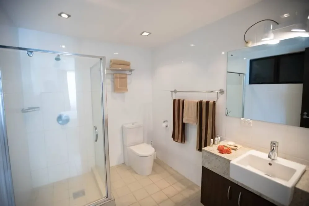 Modern bathroom with a glass shower enclosure, white toilet, towel rack with brown and beige towels, mirror, sink with a countertop, and bathroom accessories.