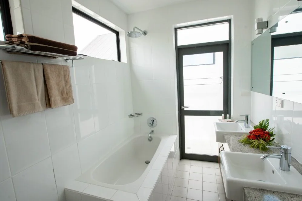 Modern white bathroom with bathtub, two sinks, towel rack, and natural light from windows