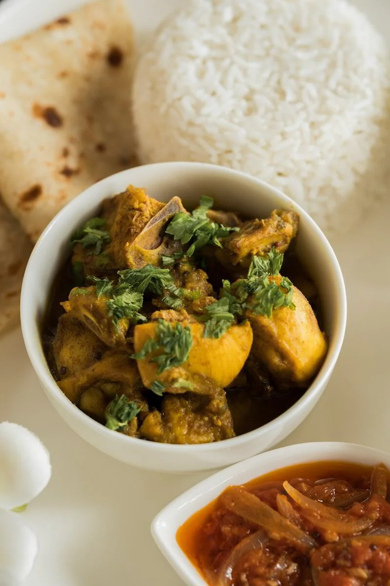 Indian meal with rice, chicken curry garnished with cilantro, naan bread, and a side of tomato-based vegetable curry.