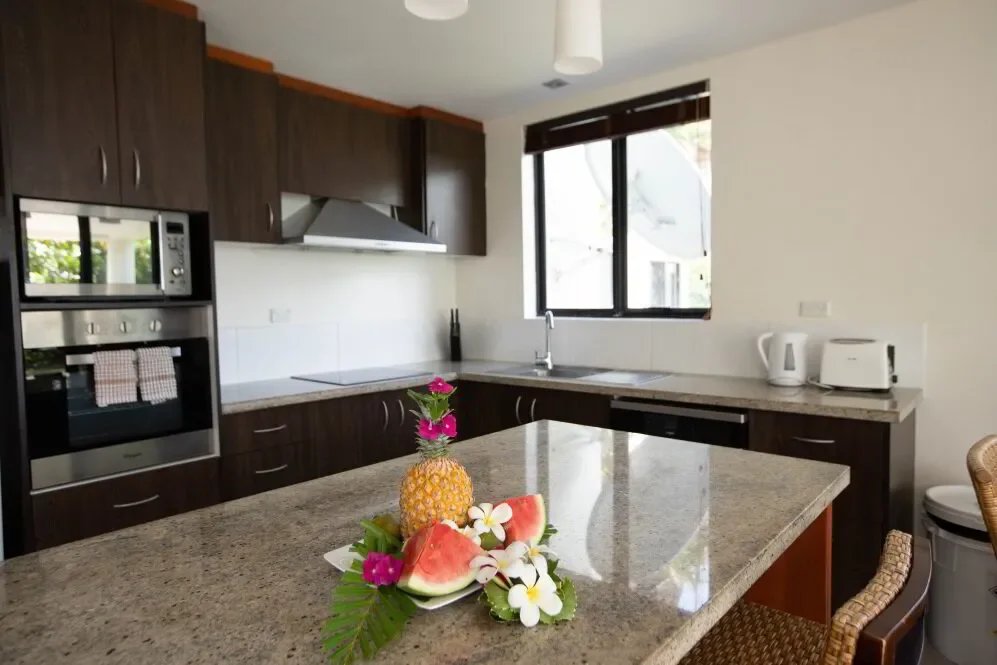 Kitchen with dark wood cabinets, granite countertops, microwave, oven, and window. Fruit and flowers on the counter.