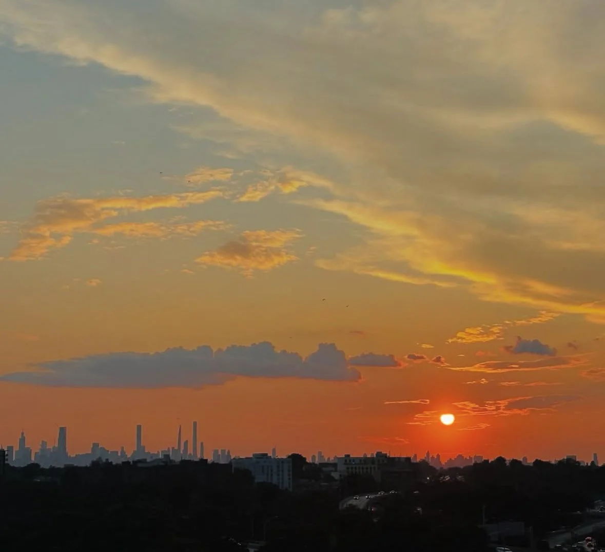 Sunset over a city skyline with clouds and colorful sky.