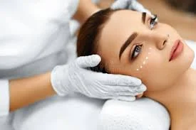 A woman receiving a facial treatment, lying back with a beautician applying skincare product near her face.