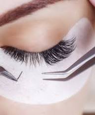 Close-up of a person with closed eye, long false eyelashes, and a white face mask, with tweezers holding eyelash extensions.