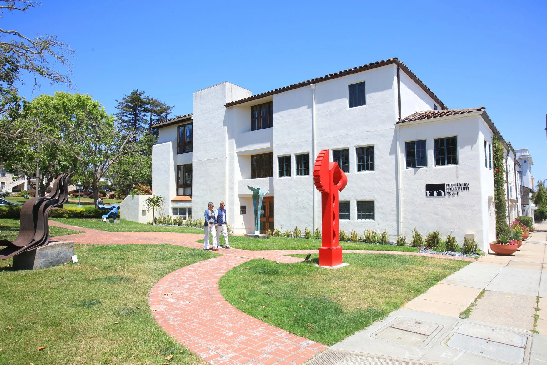 Exterior of the Monterey Museum of Art building with sculptures and visitors in the landscaped garden.