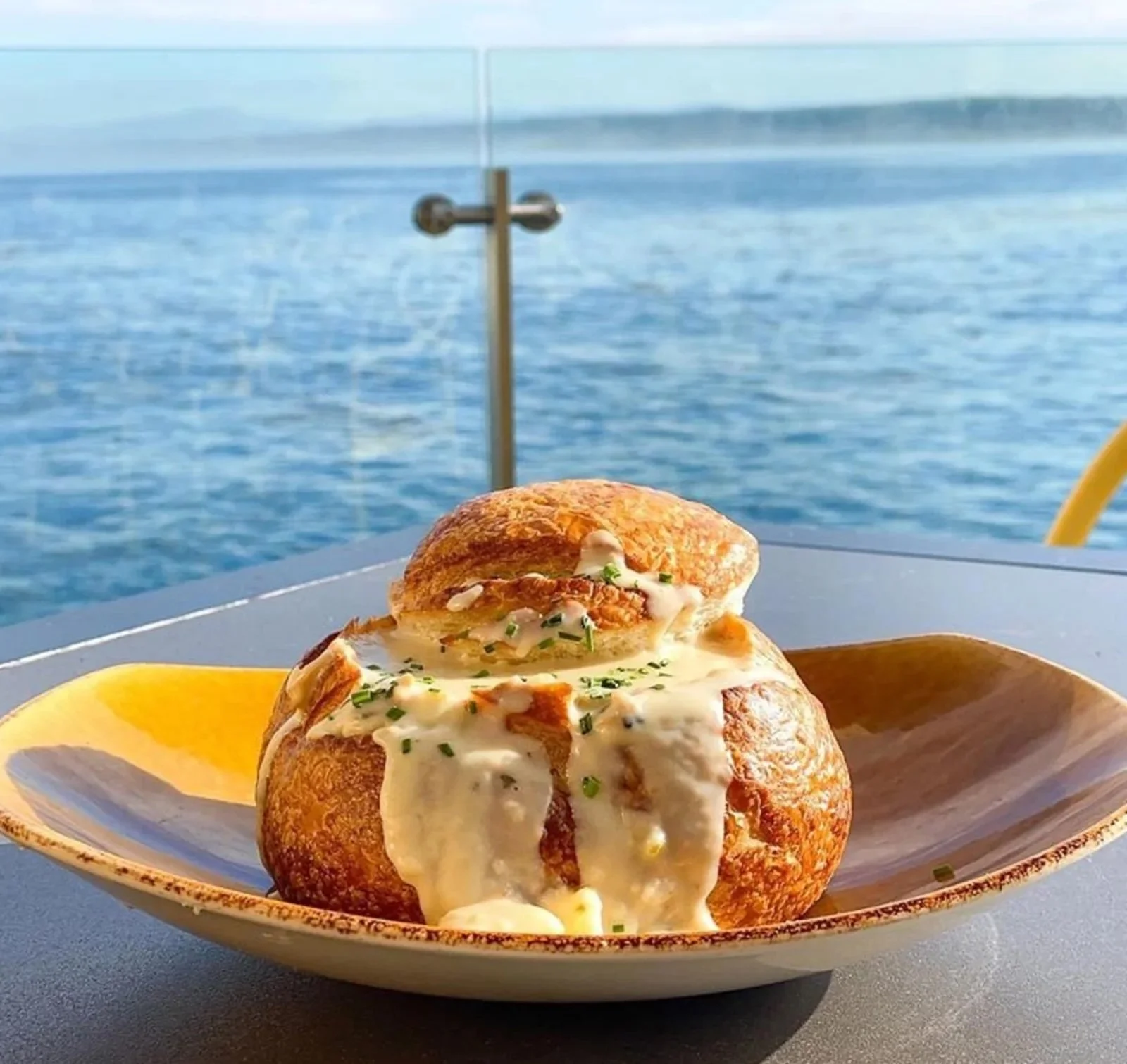 A meal featuring baked stuffed mushrooms topped with cheese and chopped herbs, served on a yellow plate with ocean view in the background.
