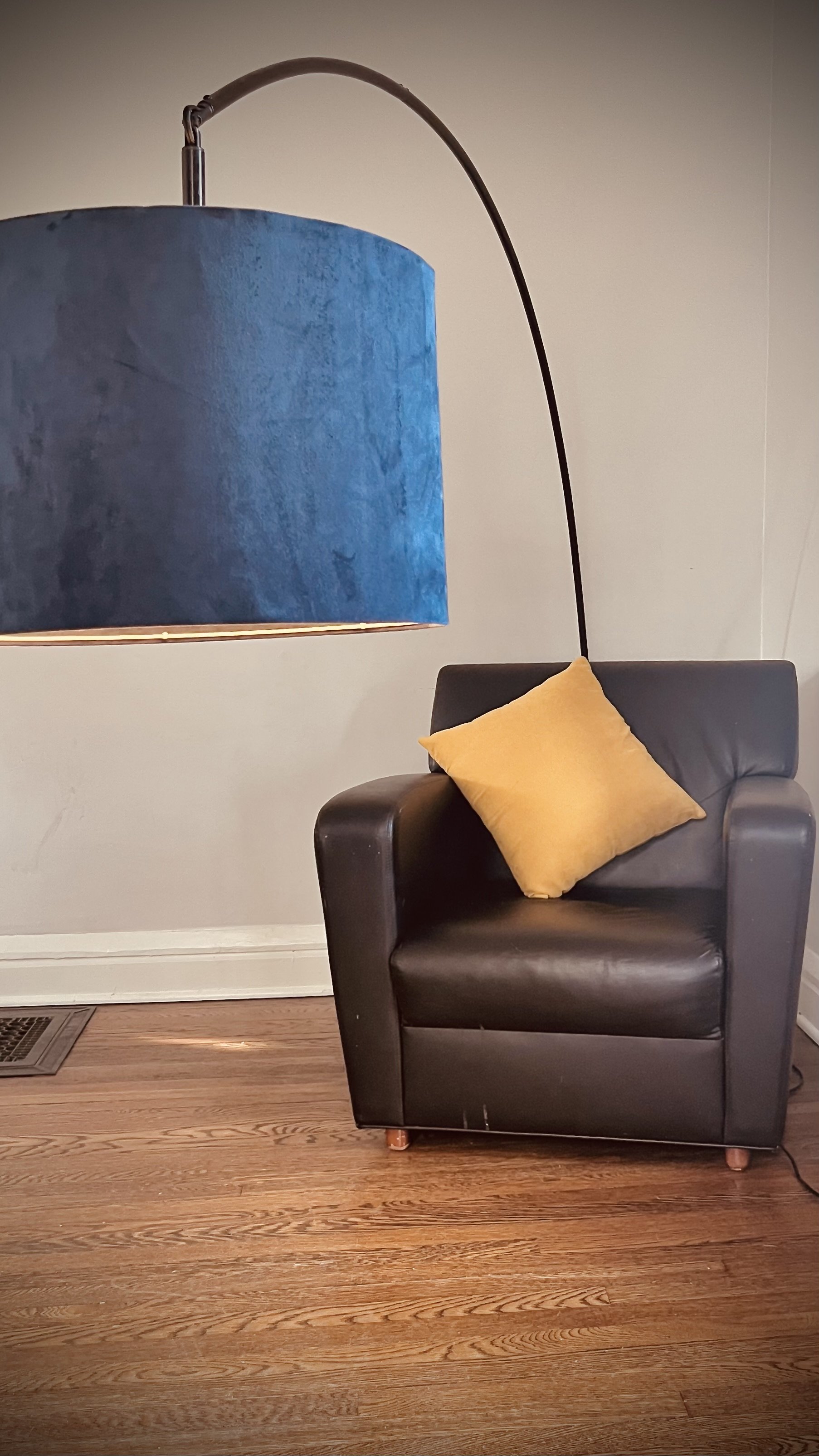 A black leather armchair with a yellow pillow on it, situated on a wooden floor next to a wall.
