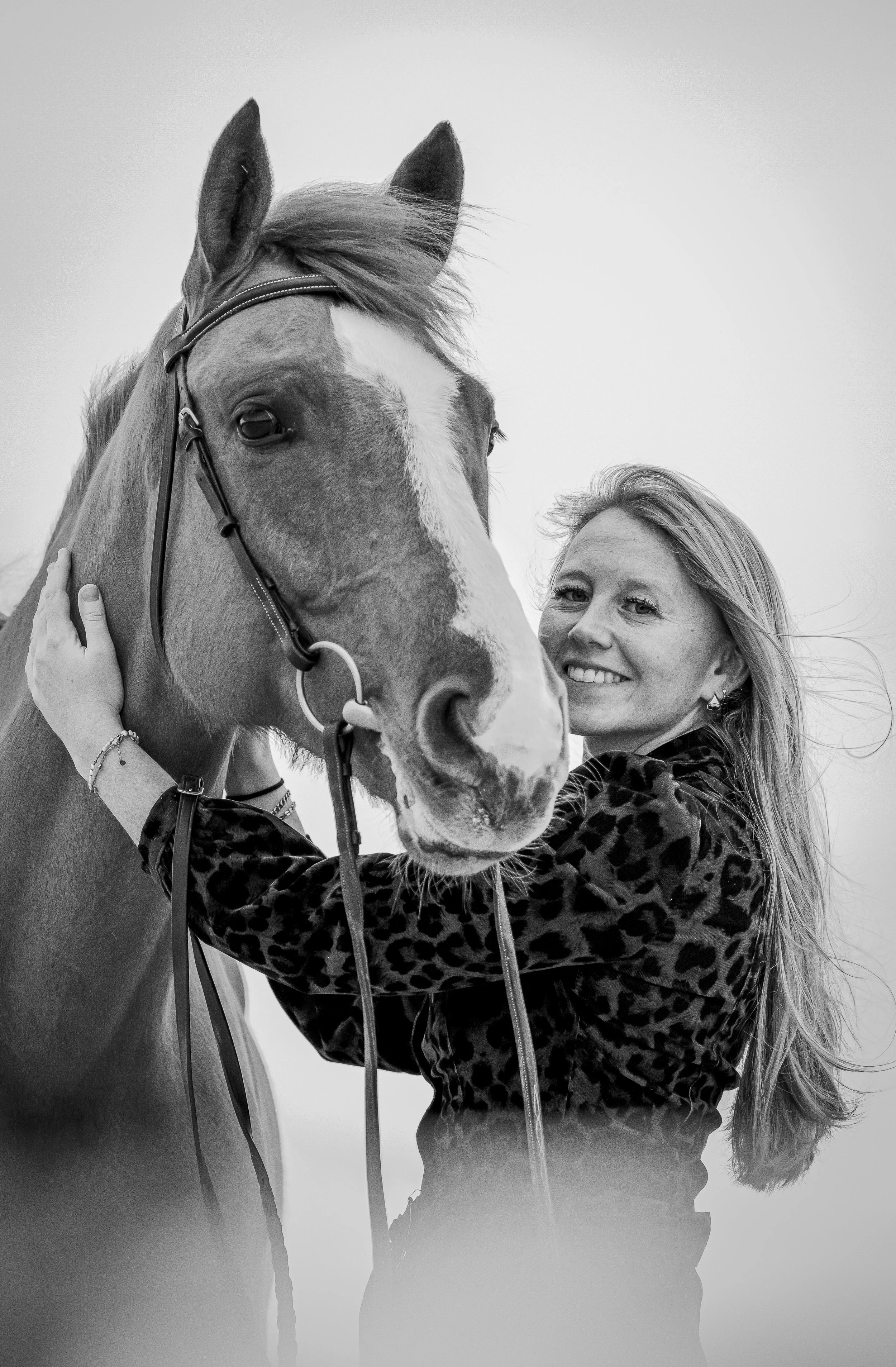Woman smiling while holding her horse — natural black-and-white equine portrait.