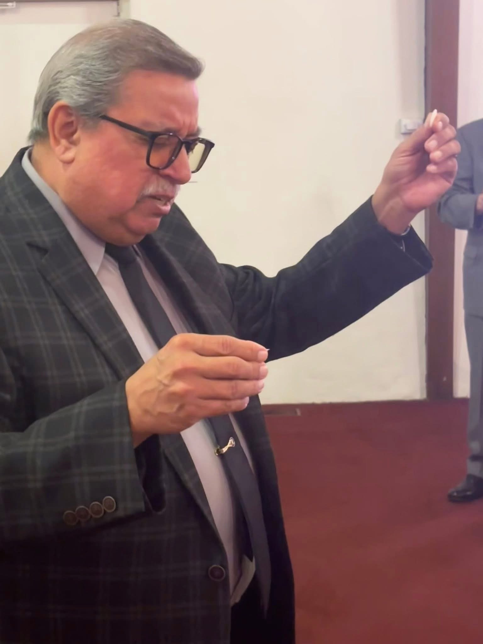 An older man with gray hair and glasses praying with his eyes closed and hands raised.