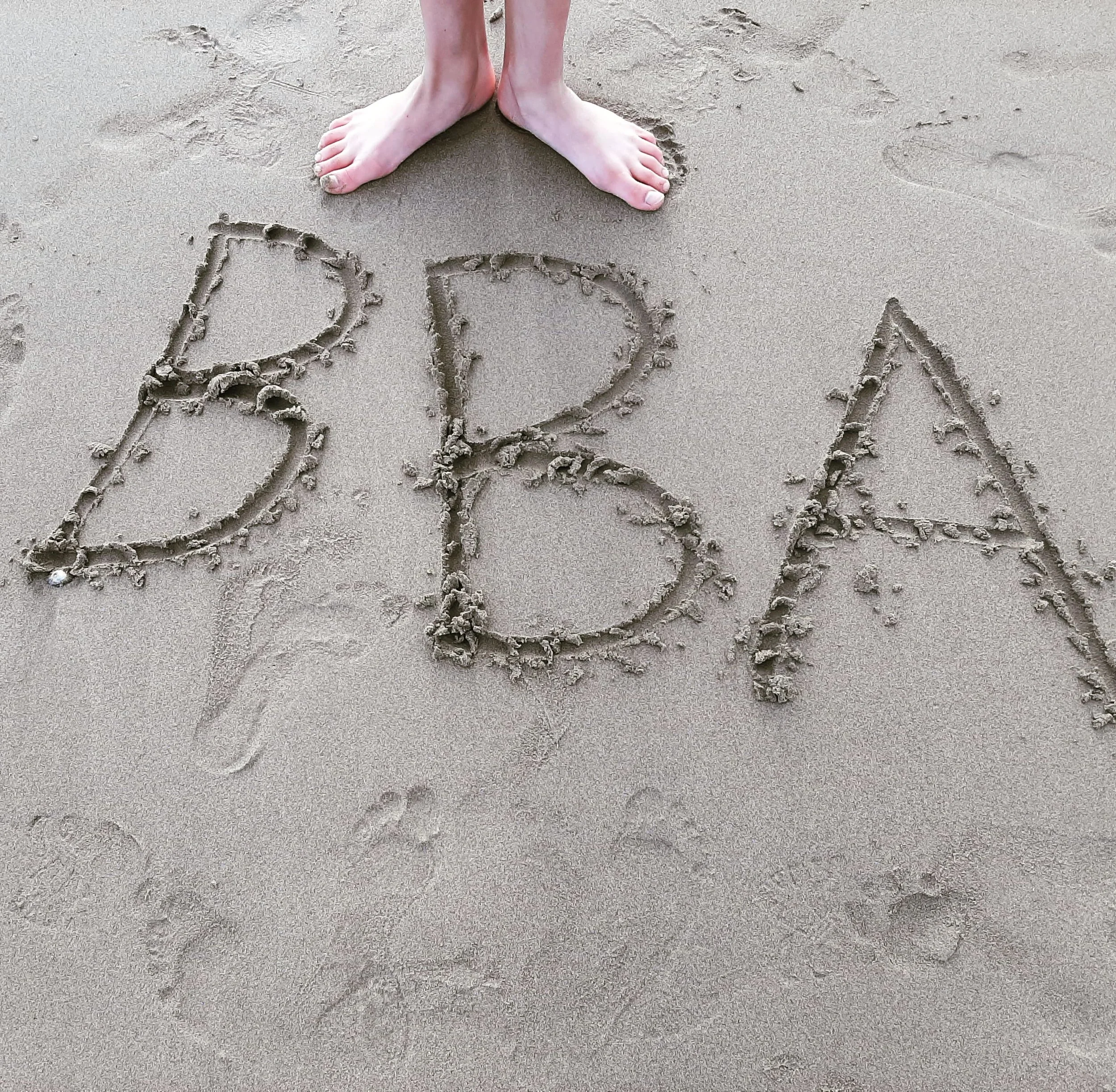 Person standing on sand with the word "BAB" written in the sand.