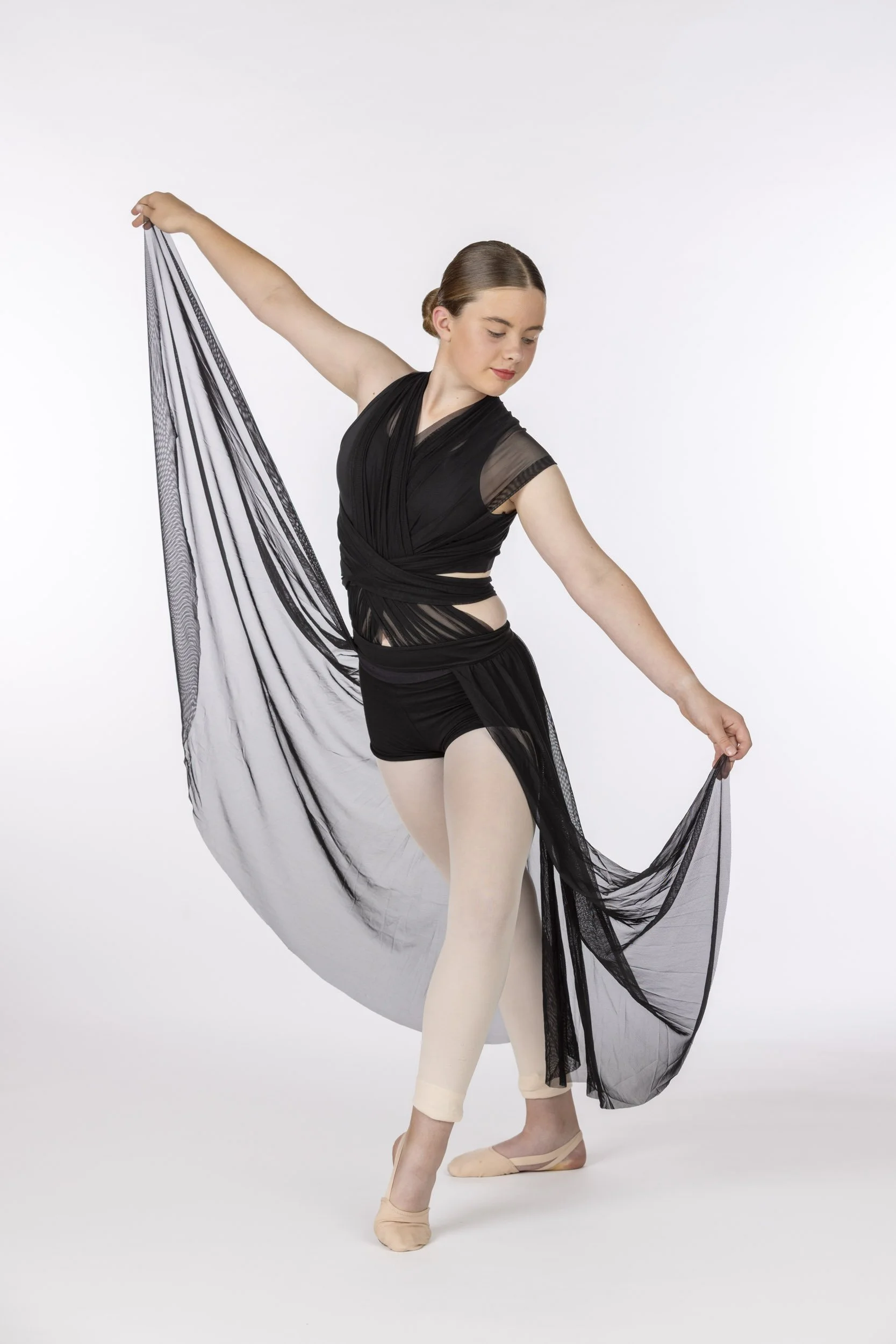 Ballet dancer in black costume posing with a sheer black fabric against a plain white background.