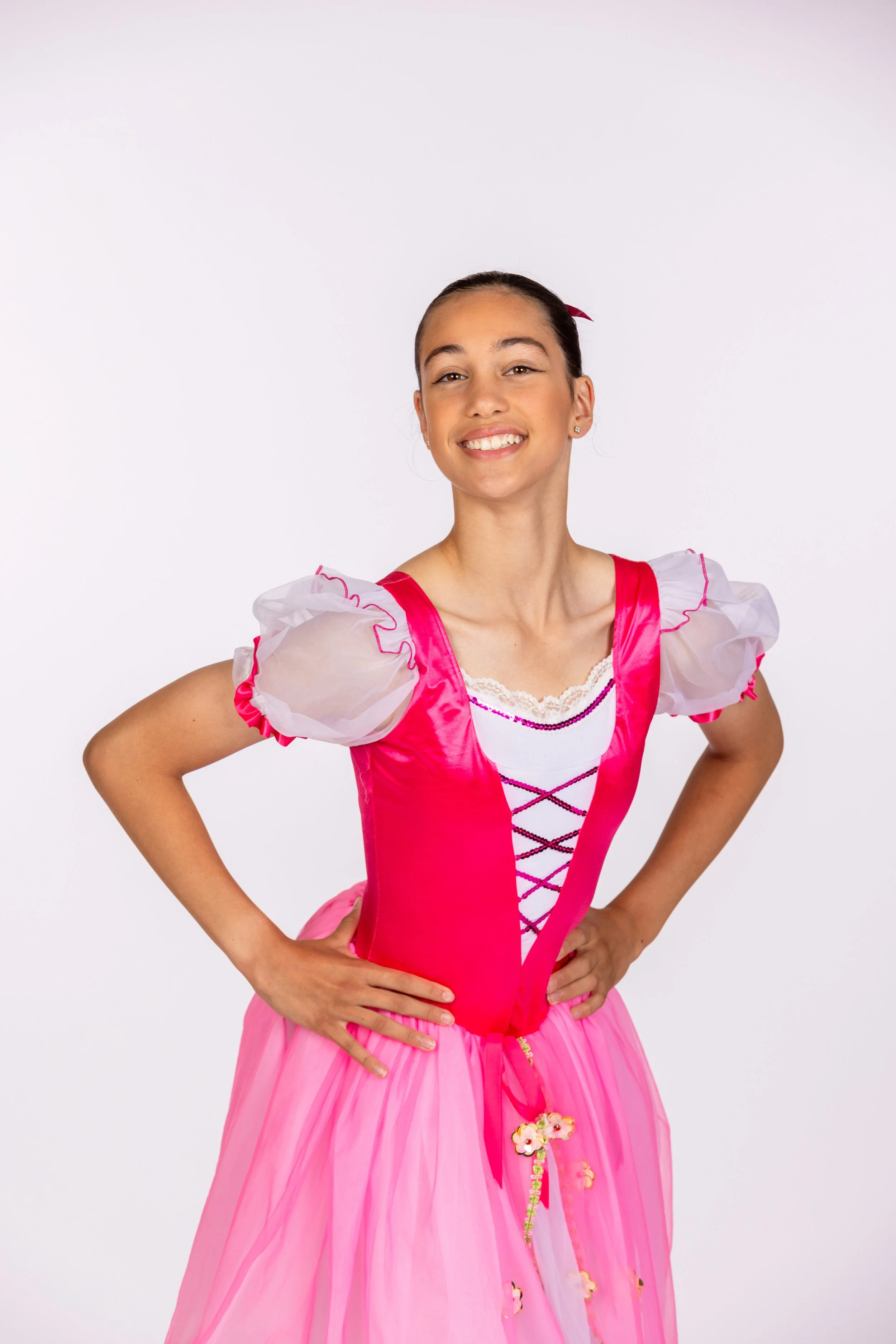 Young girl in a pink costume smiling with hands on her hips against a plain white background.
