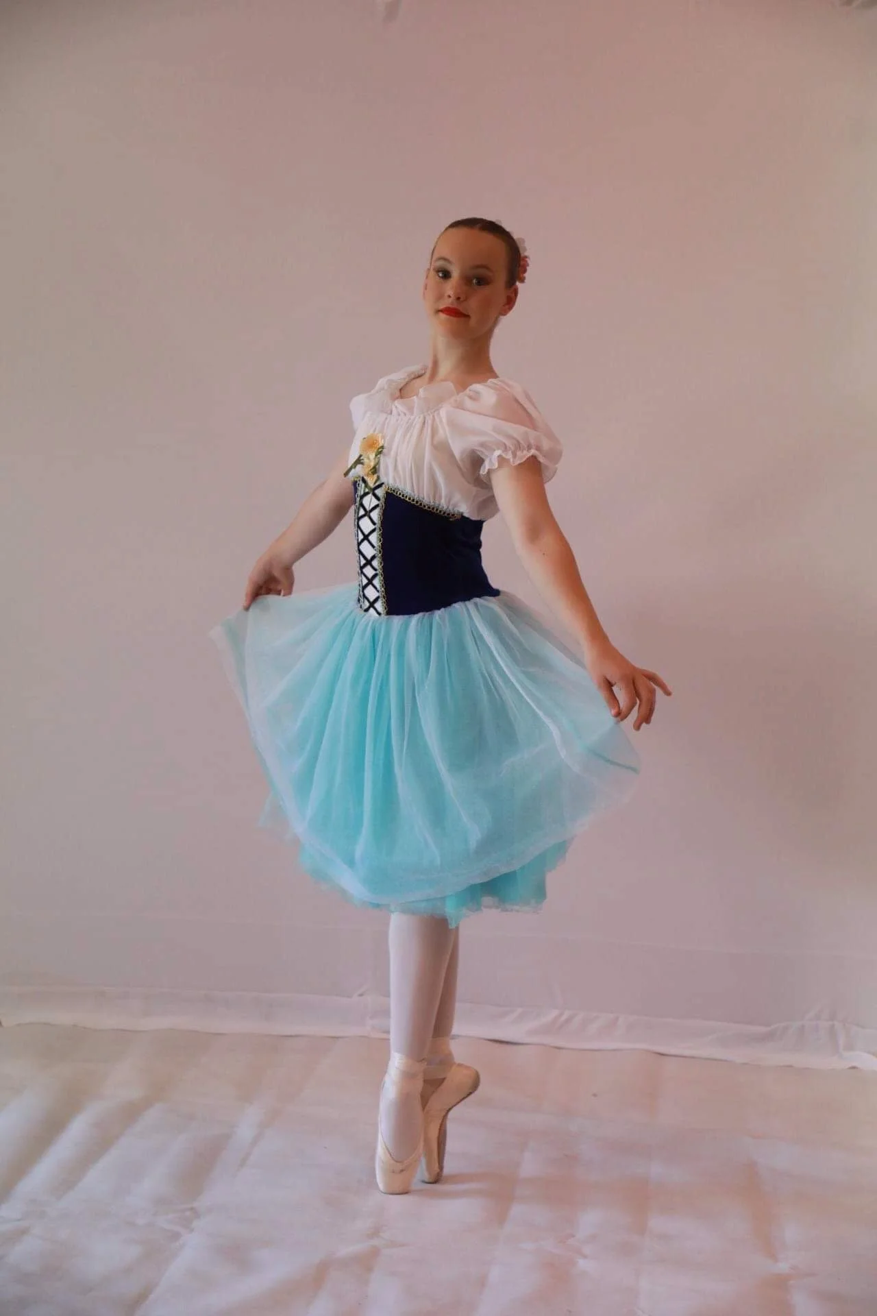 Young girl ballet dancer in a costume, standing on pointe in a tutu, with a pink background.