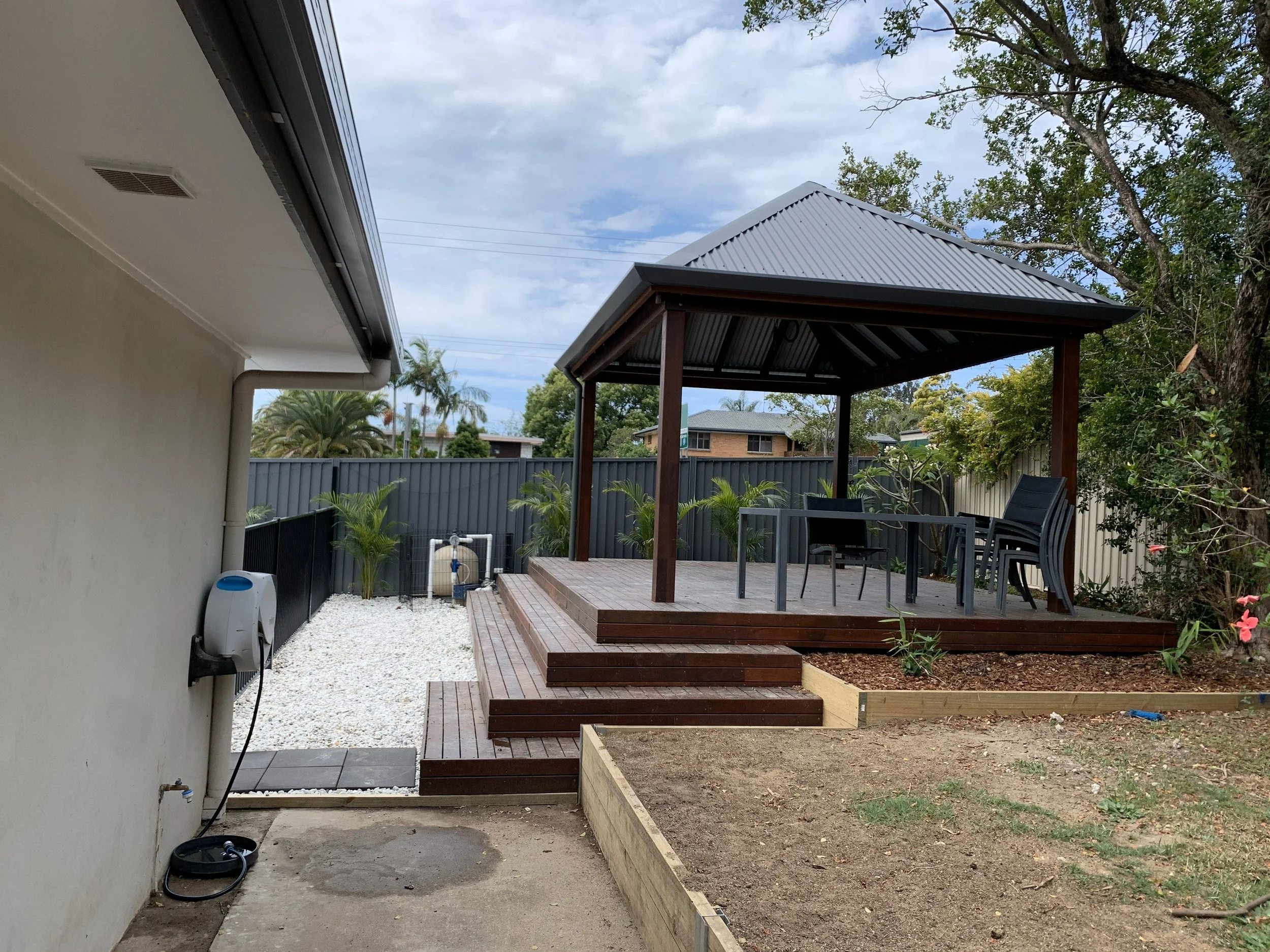 Backyard with a wooden deck and a gazebo, outdoor furniture, and a garden area with plants and trees.