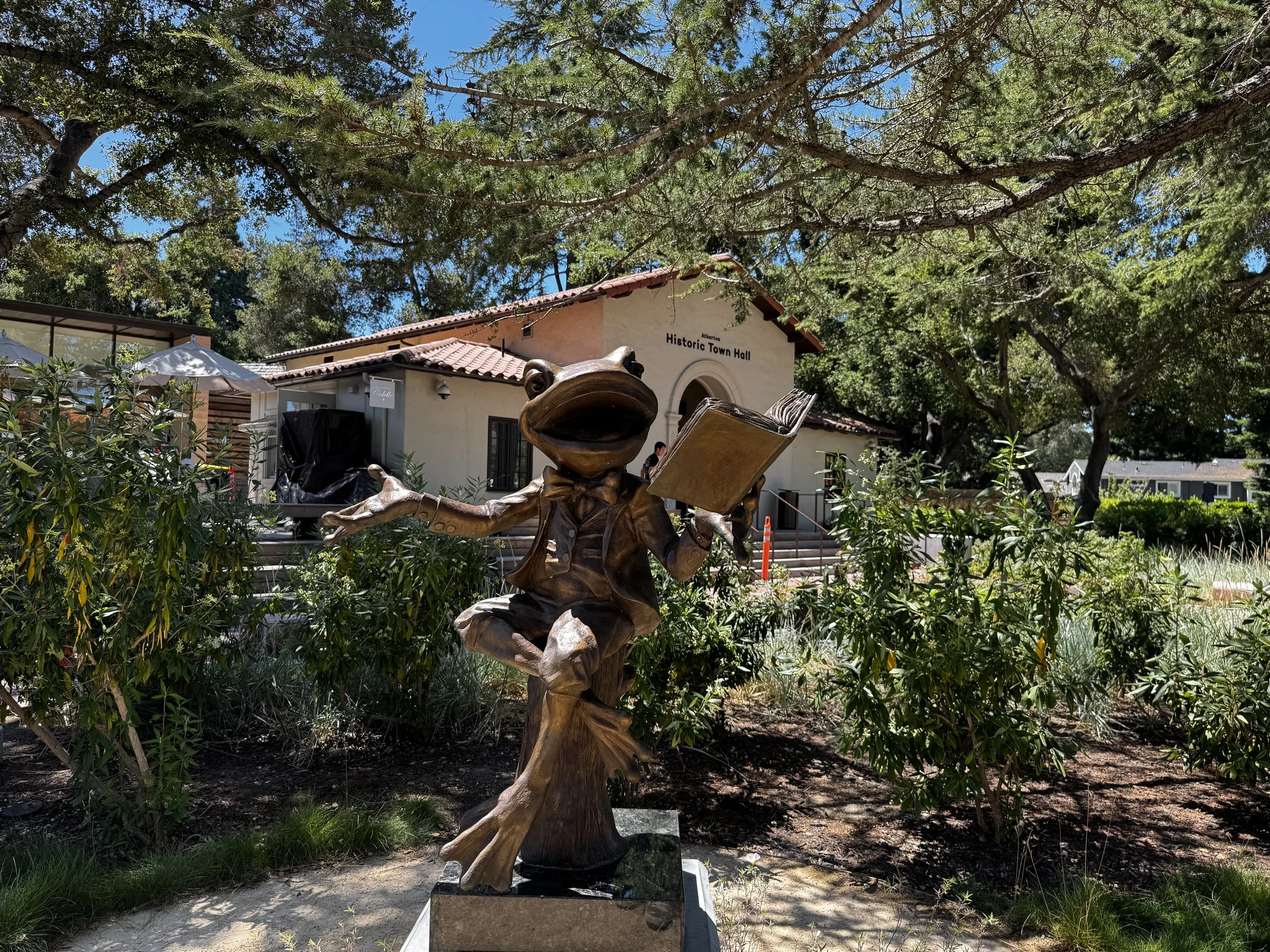 Bronze frog statue in front of the Atherton Library, with the Atherton Historic Town Hall in the background.