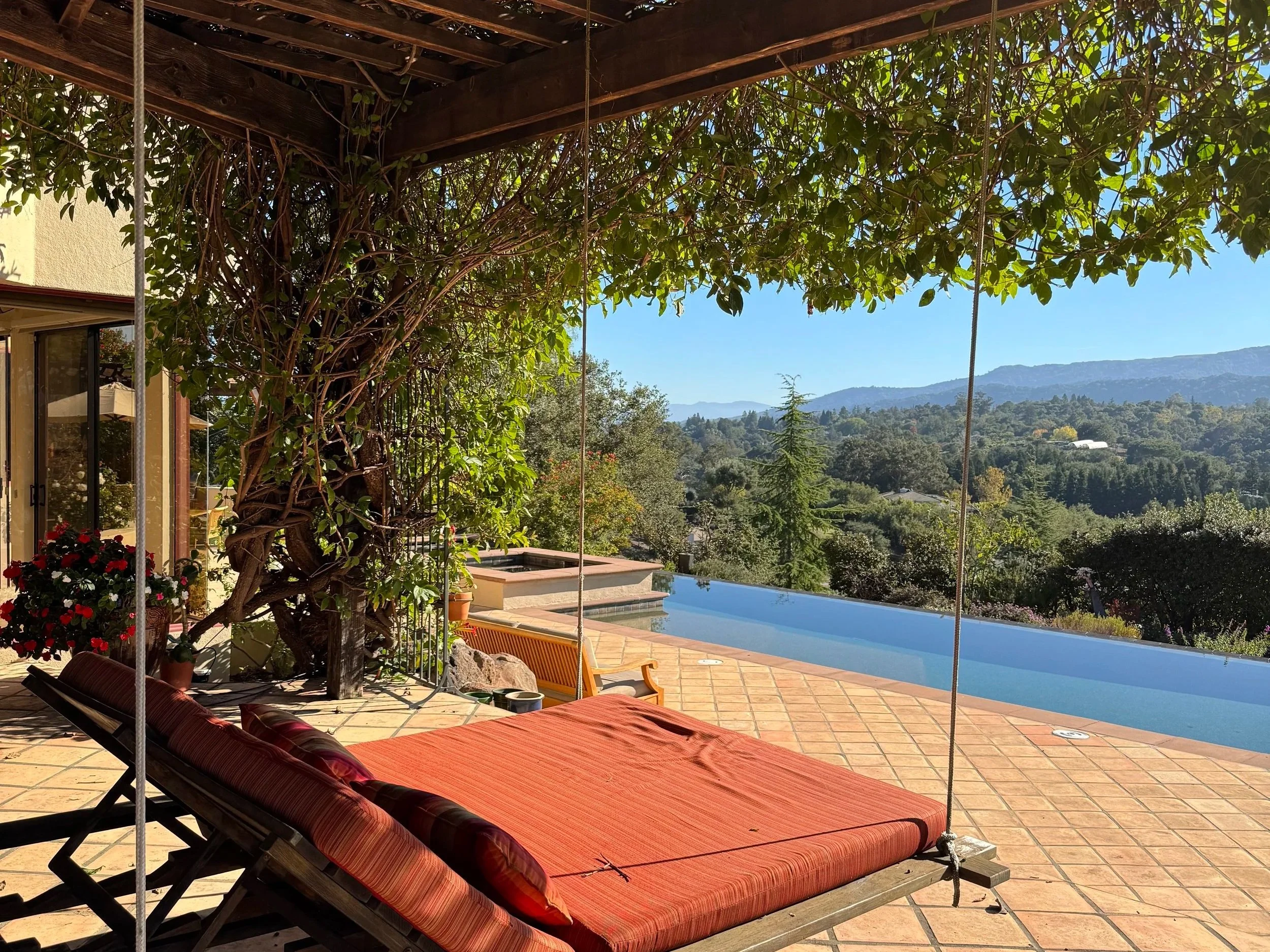 Backyard of a luxury Los Altos Hills estate with a pergola lounge, infinity pool, spa, and expansive hillside views.