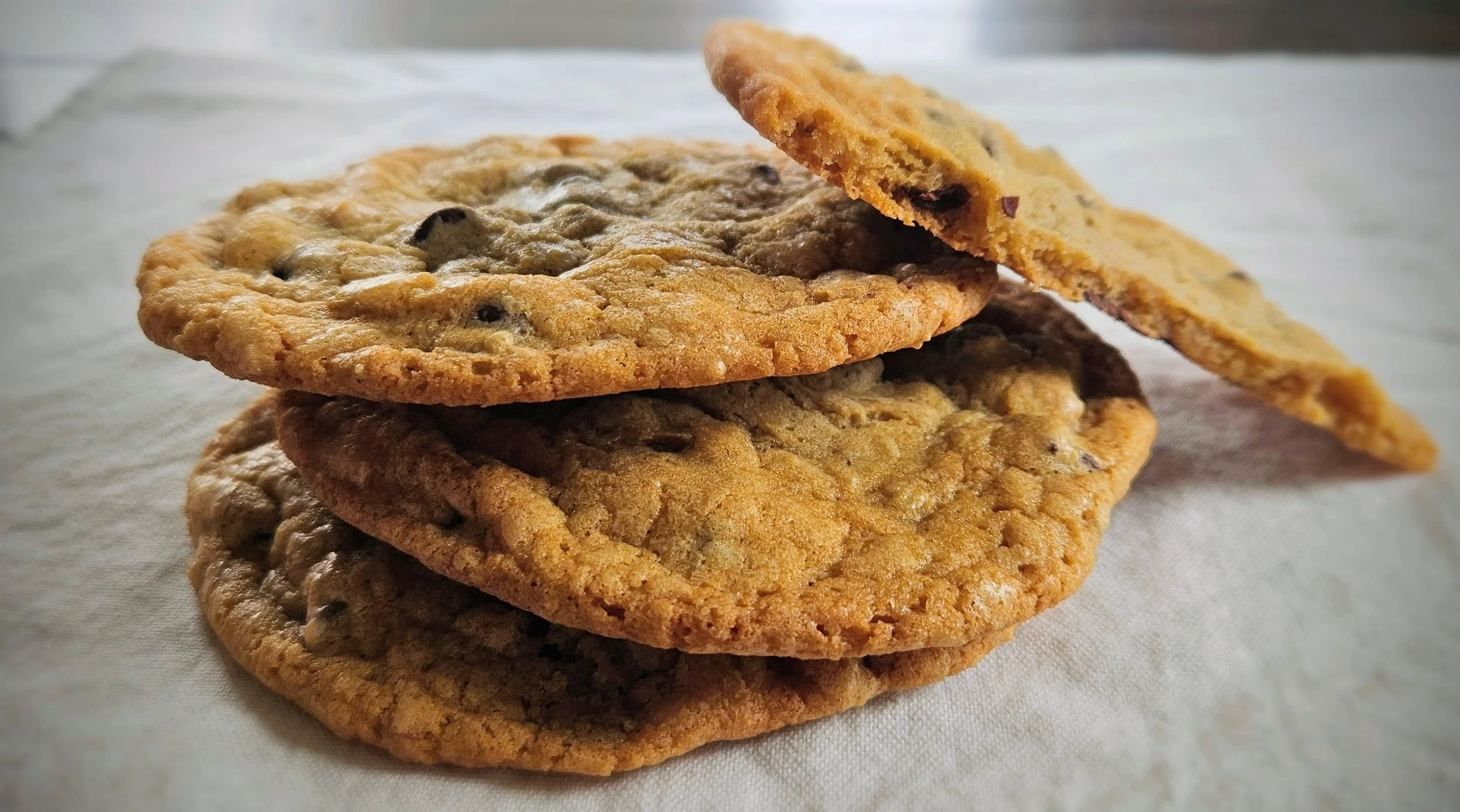 Oversized crispy-edge chocolate chip cookies stacked on parchment, 4-pack and 6-pack available — Hauber Bread and Baking, order online Antioch IL