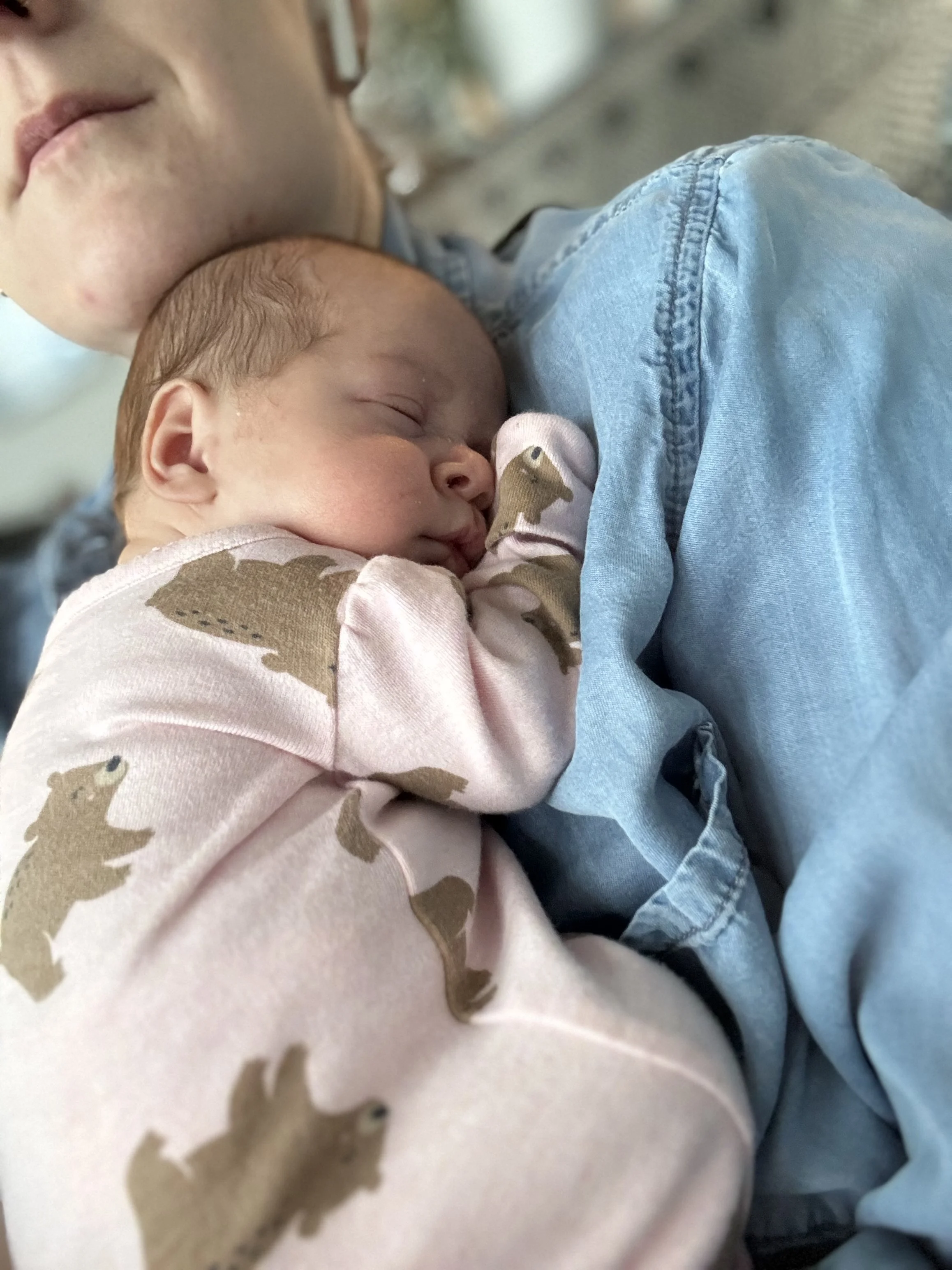 A baby asleep on an adult's chest, wearing a pink onesie with bear patterns.
