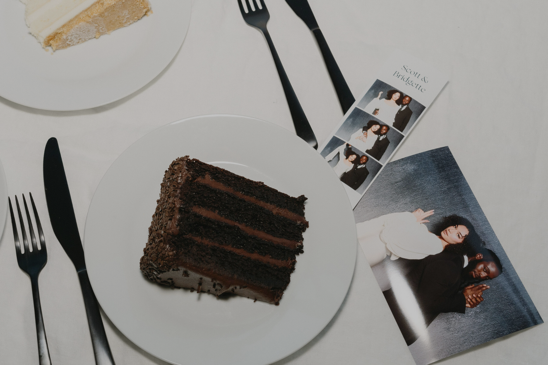 A slice of chocolate layered cake on a white plate, with black utensils beside it, and a photo strip featuring a couple with the names Scott and Bridgette nearby.