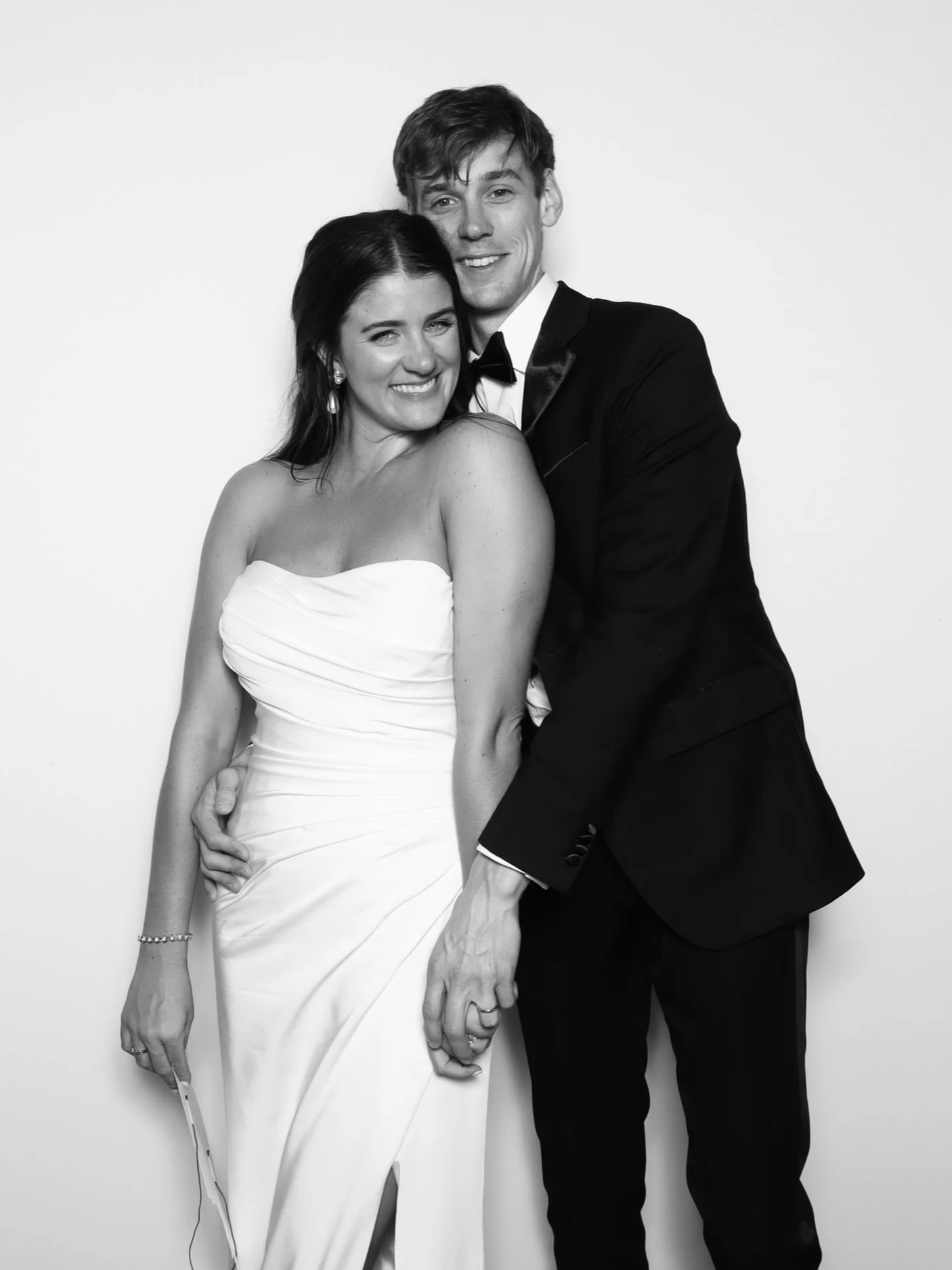 A happy couple dressed in wedding attire, the woman in a strapless wedding gown and the man in a tuxedo, hugging and smiling.