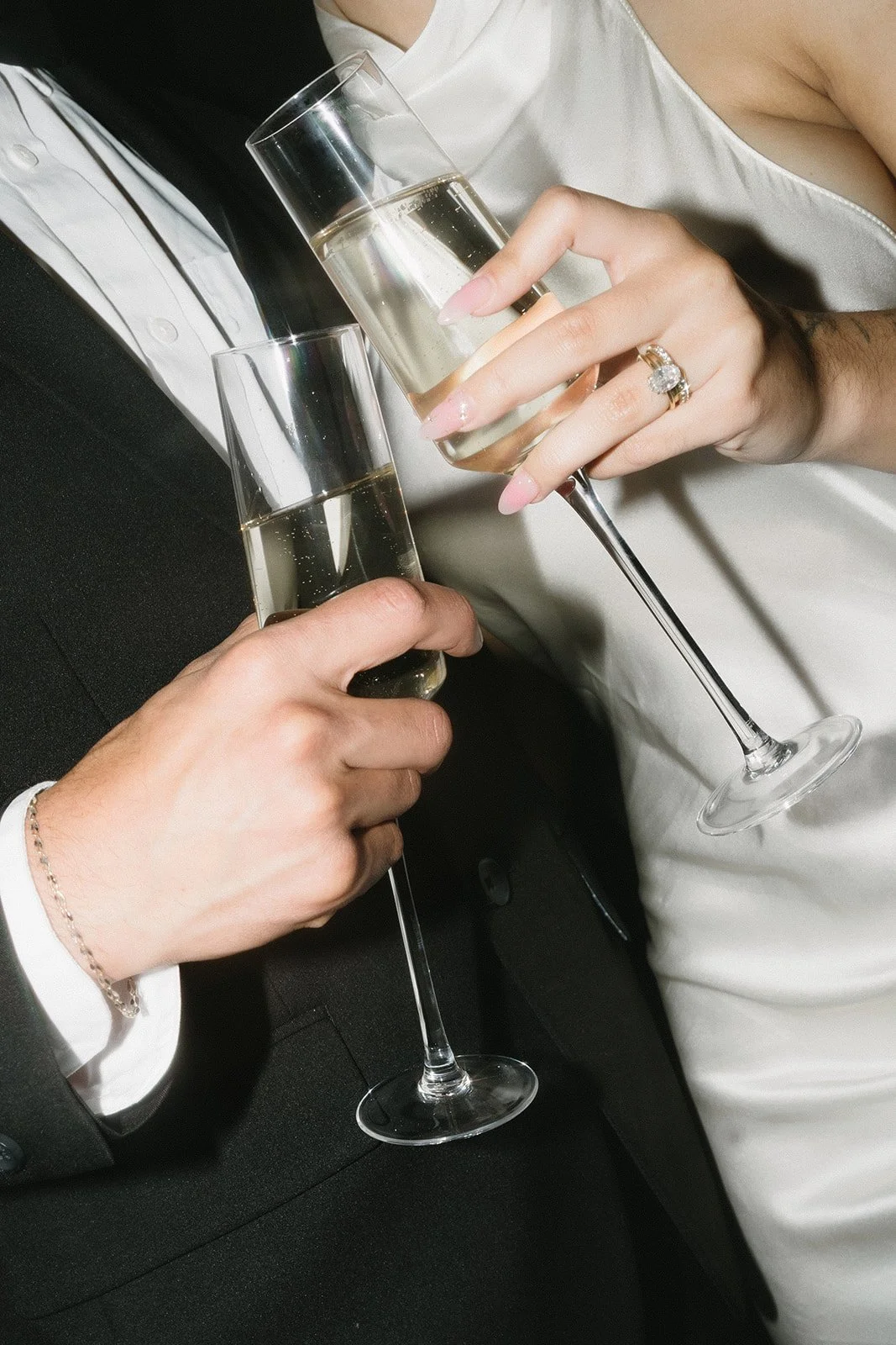 Close-up of a couple dressed in formal attire holding glasses of champagne for a toast.