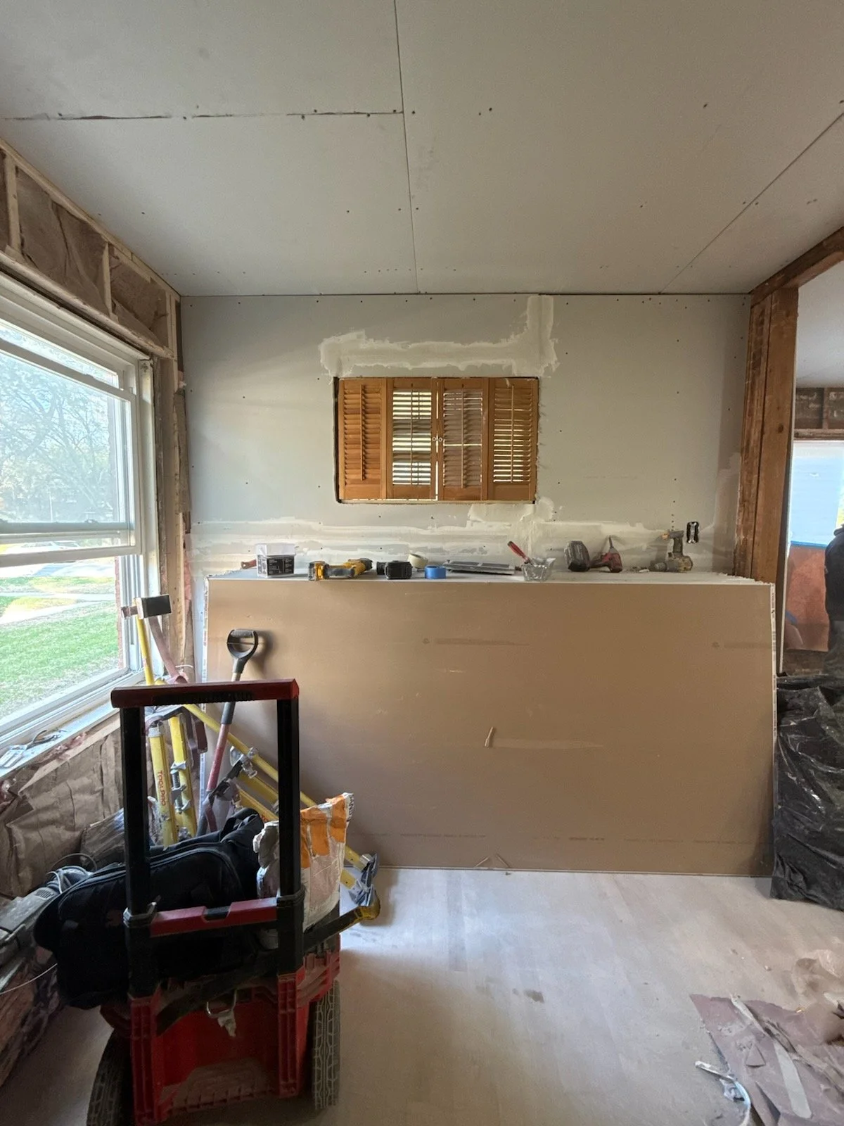 Room under construction with a window, construction tools, and plywood on the wall.