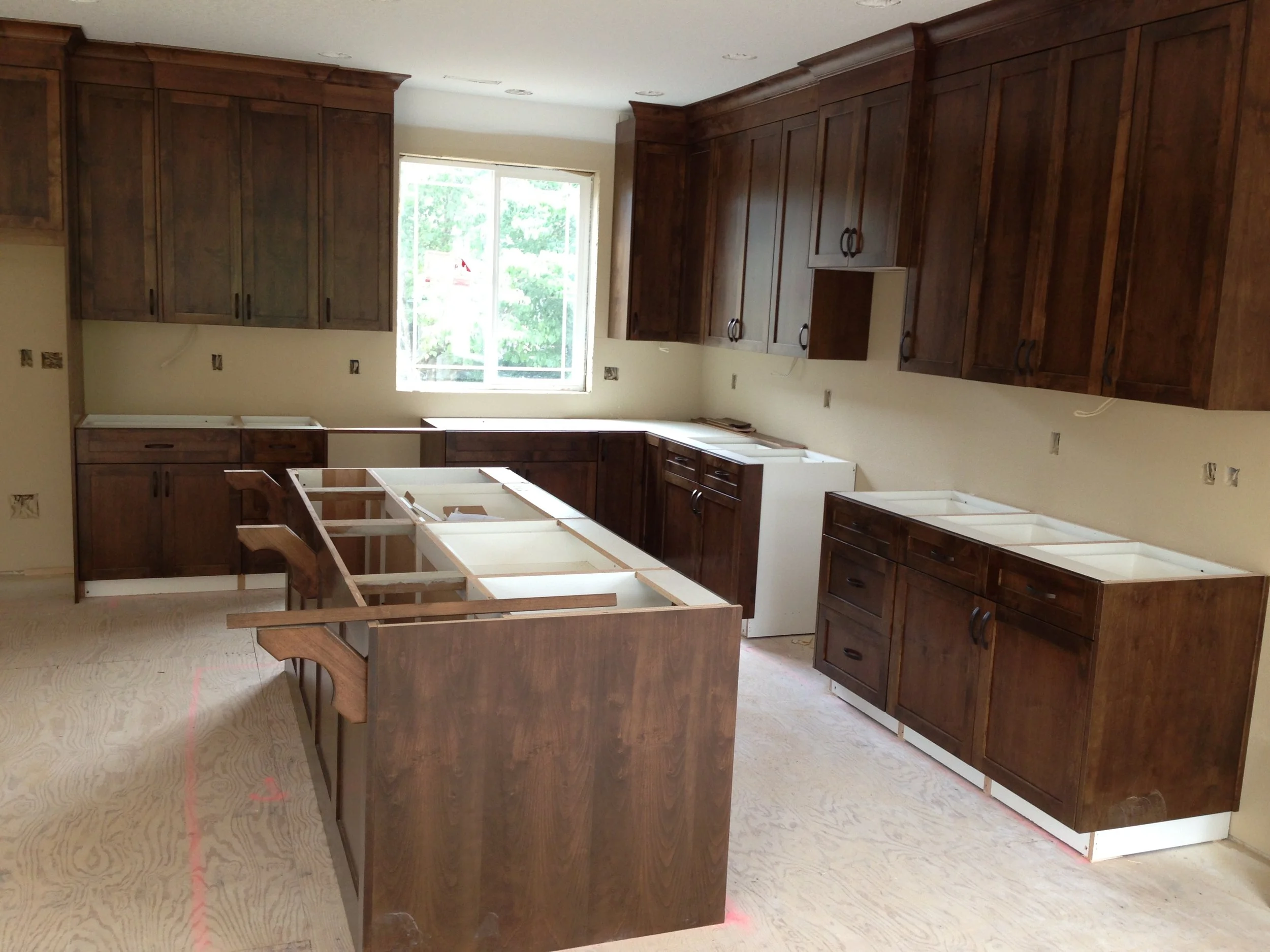 Kitchen under renovation with dark wooden cabinets, an island, and a window, construction materials on the floor.