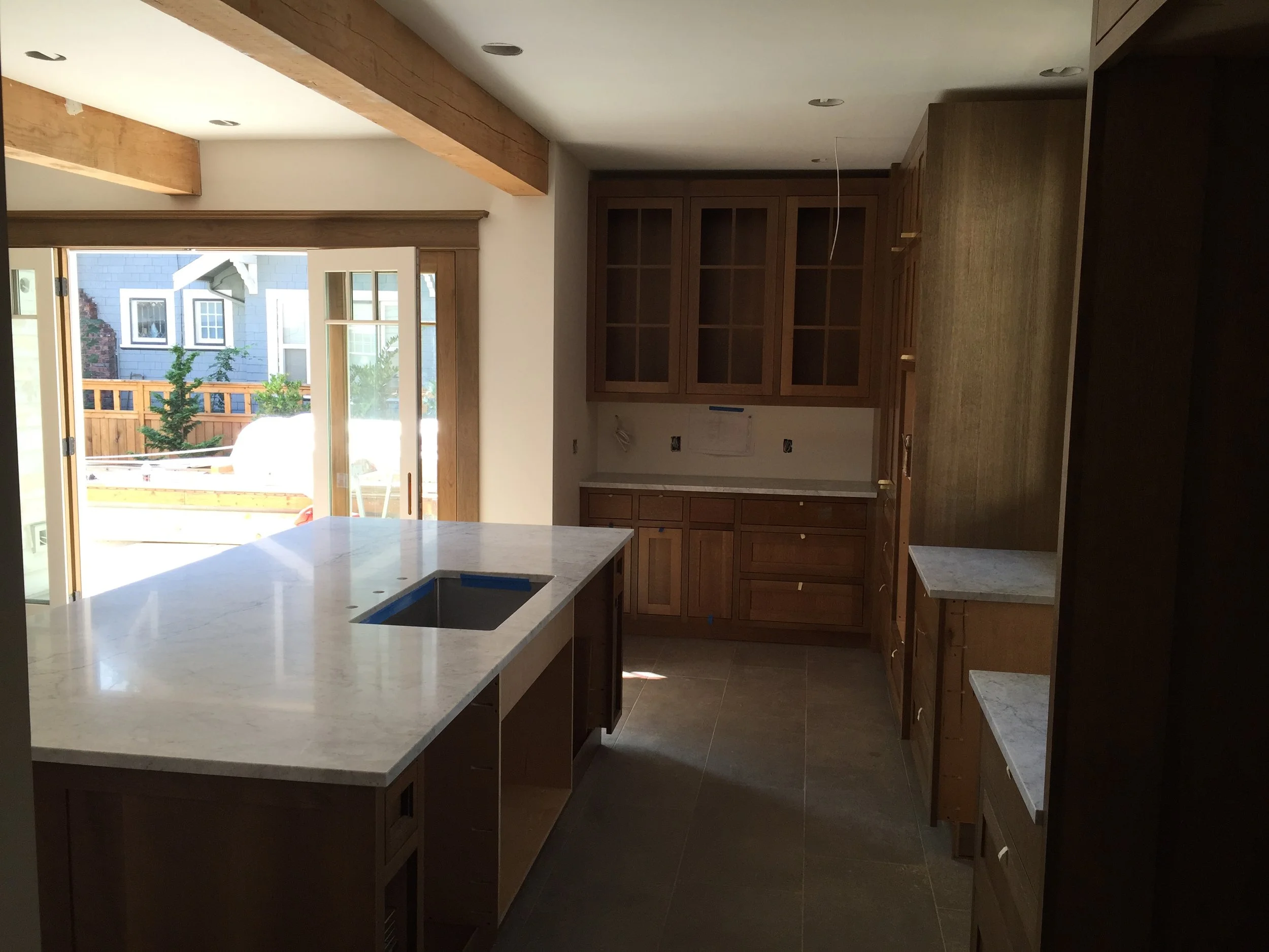 Under construction kitchen with wooden cabinets, marble countertops, and sliding glass doors leading to outdoor yard.